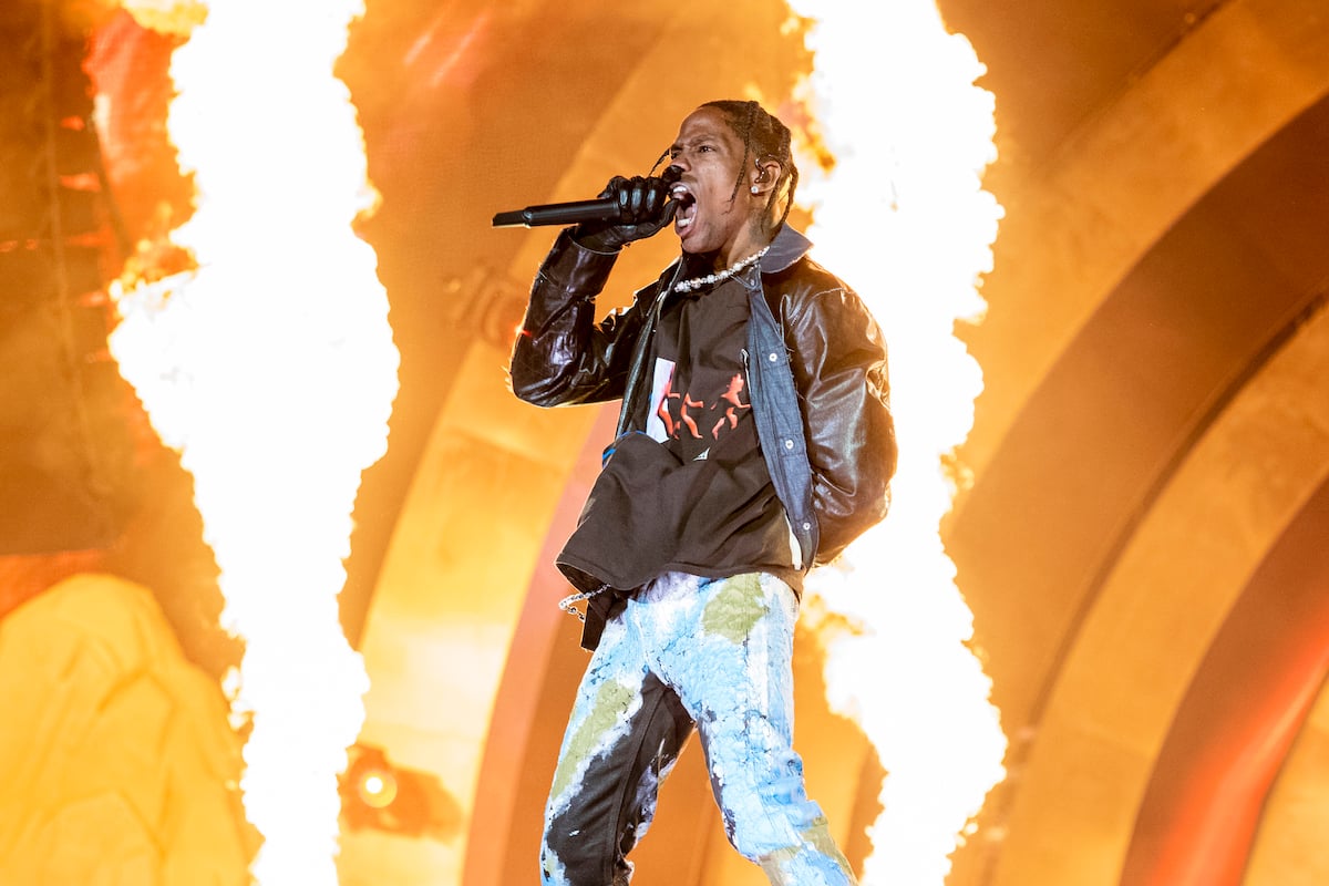 Travis Scott performs on stage with flames behind him.