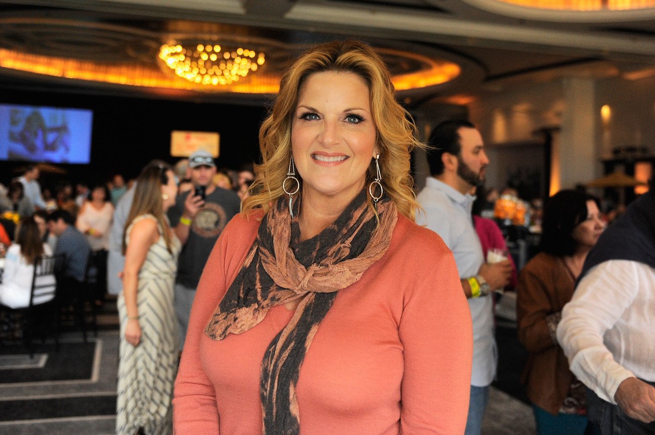 Trisha Yearwood smiles wearing a coral shirt and scarf