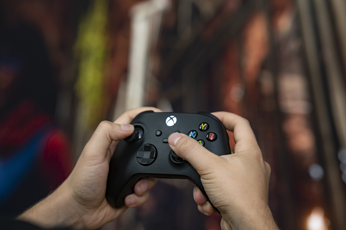 A person holding an Xbox video game controller in front of a blurred backdrop