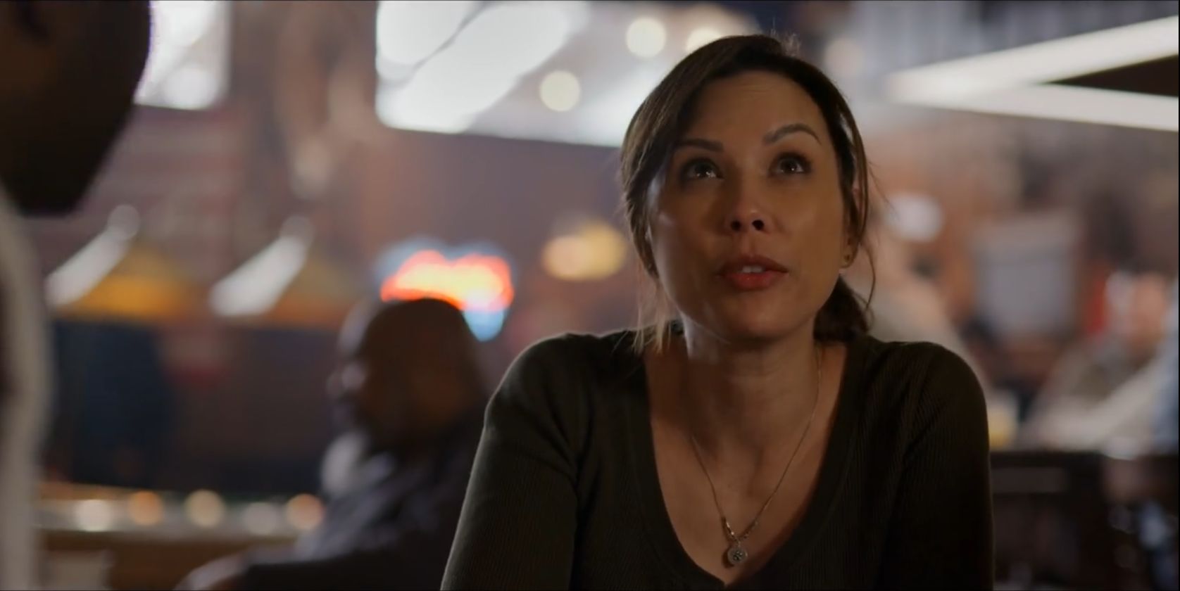 Lexa Doig as Paige sitting at a bar wearing a dark shirt in 'Virgin River'