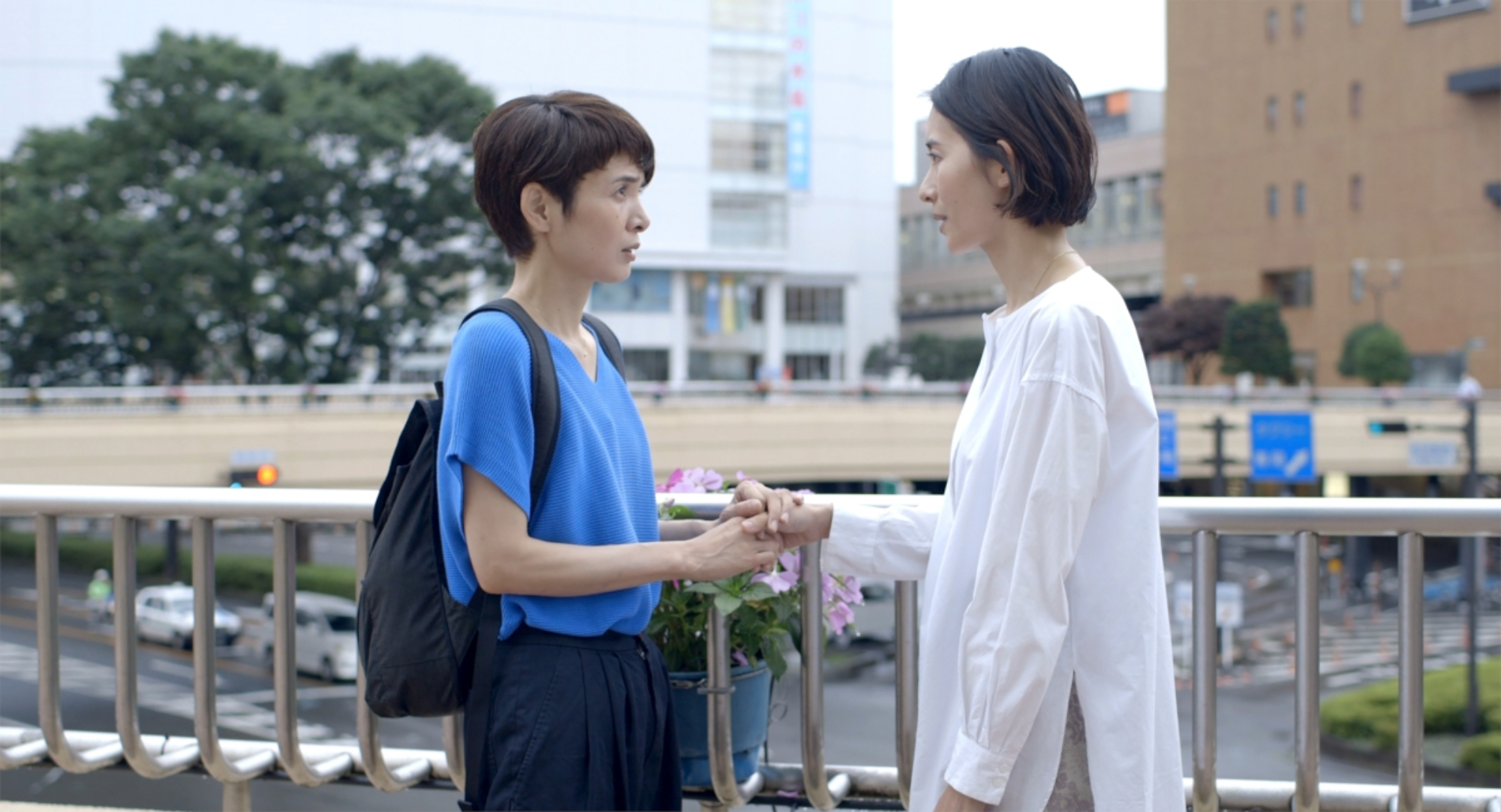 'Wheel of Fortune and Fantasy' L-R_ Fusako Urabe as Moka Natsuko and Aoba Kawai as Nana Aya holding hands and looking at each other in front of a railing