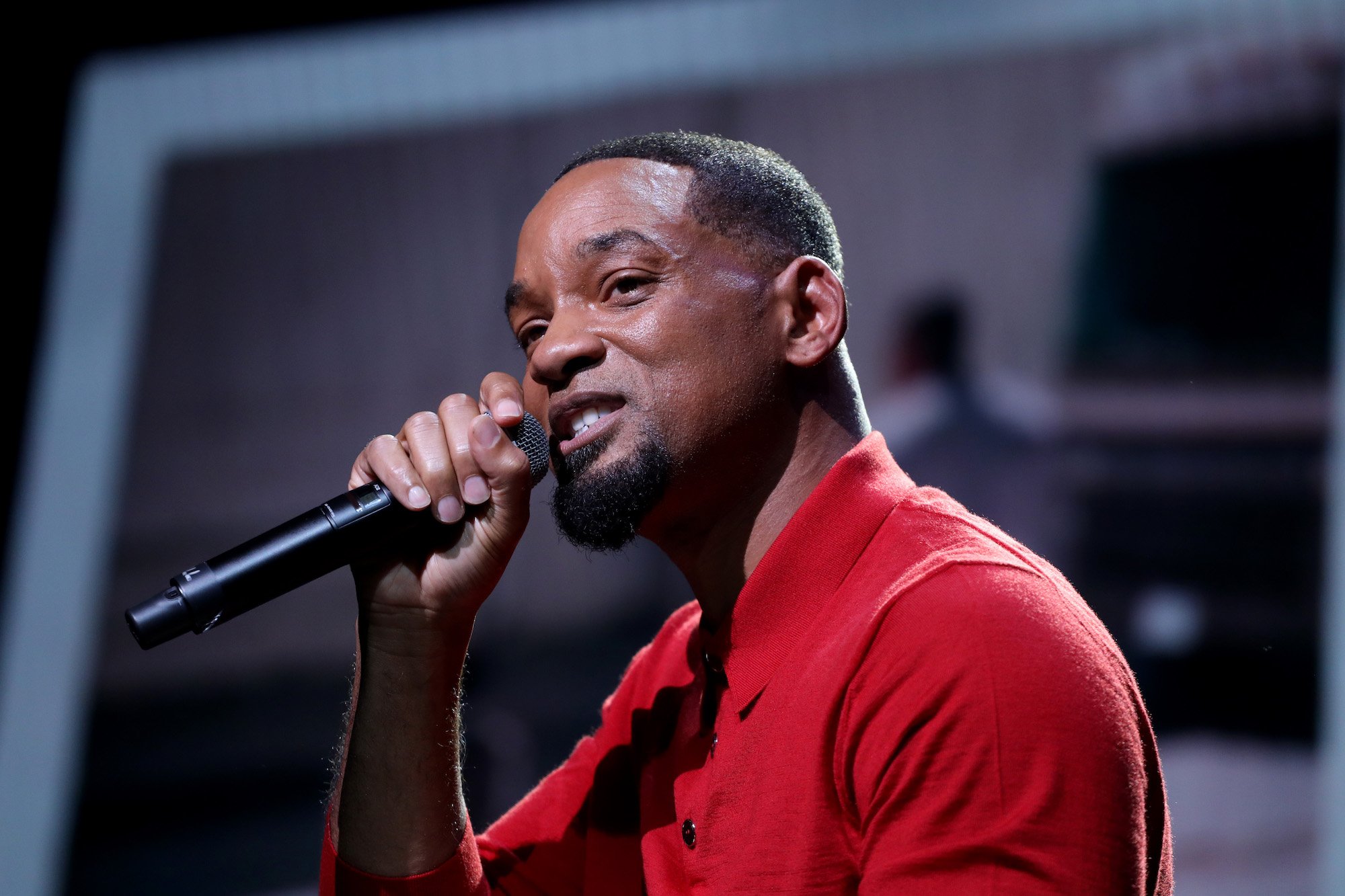 Will Smith speaks into a microphone wearing a red shirt