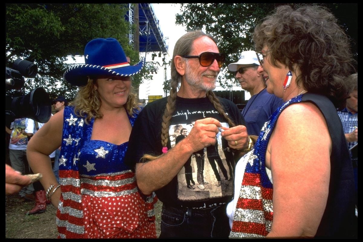 Willie Nelson (center) in sunglasses and signature braids, between two women in American flag attire