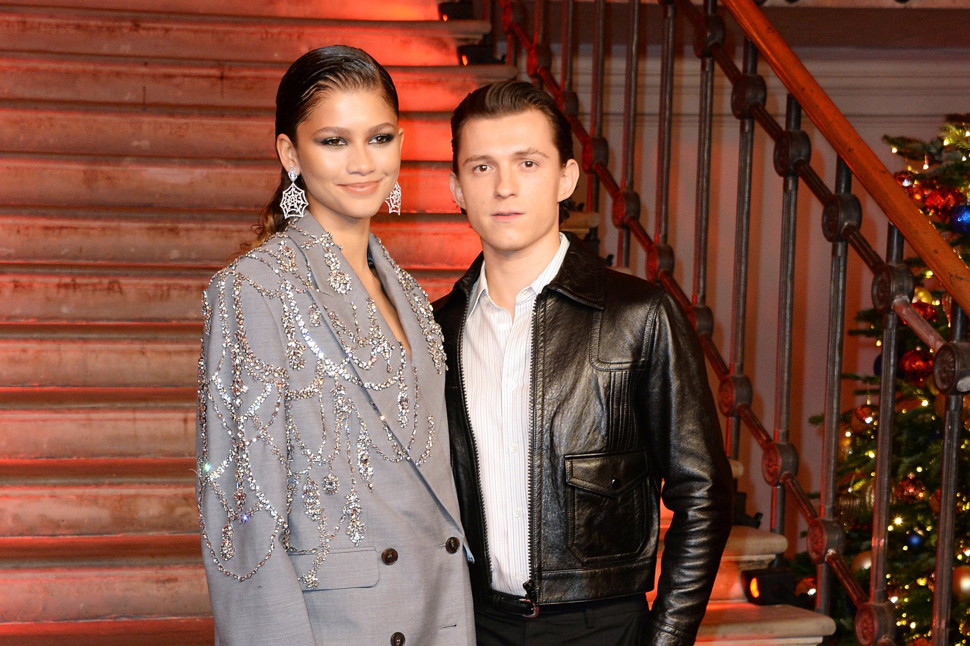 Zendaya and Tom Holland attend the photocall for 'Spider-Man: No Way Home.' She's wearing a grey blazer, and he's wearing a white T-shirt and leather jacket.
