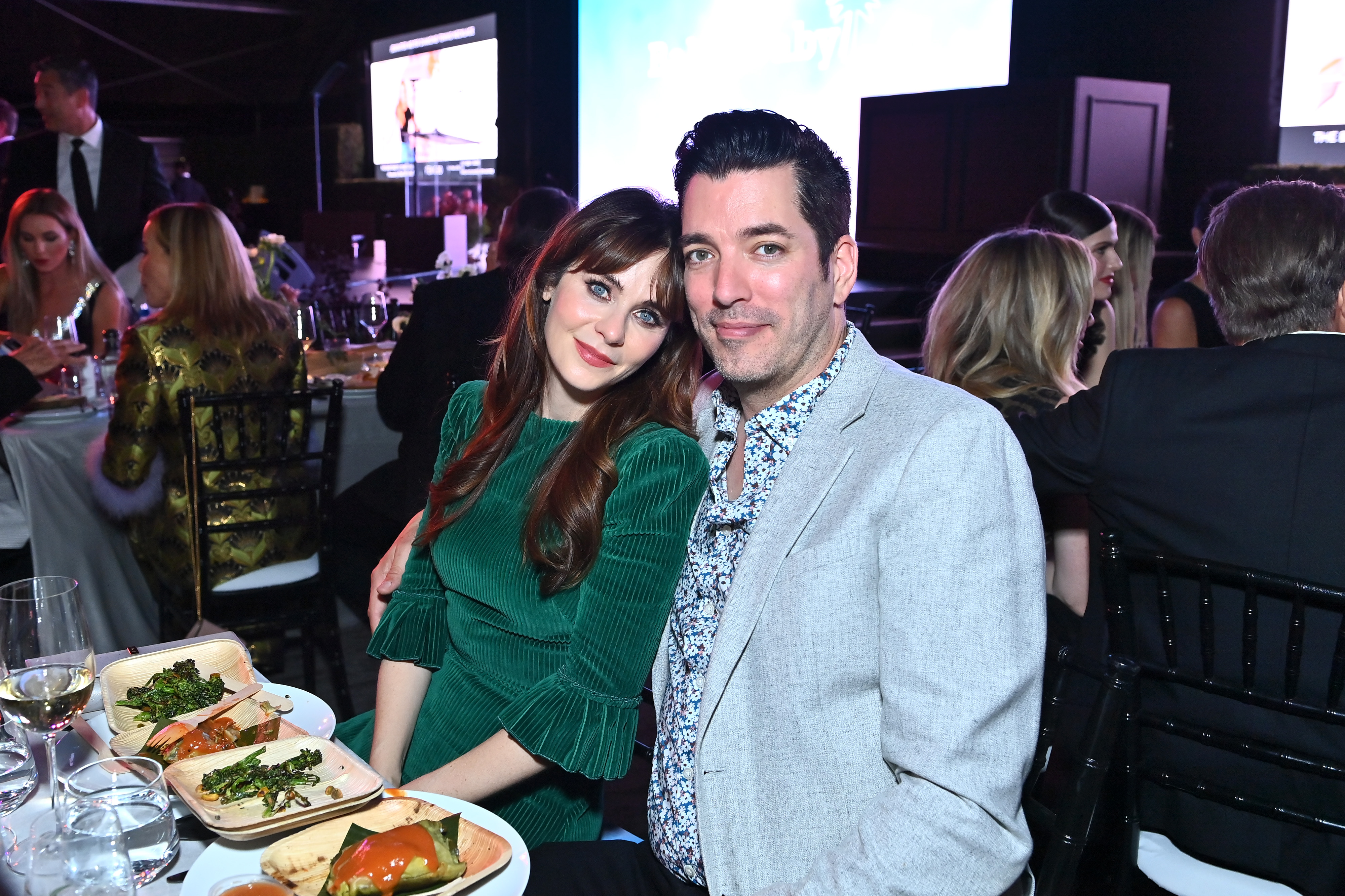 Zooey Deschanel wearing a green dress poses with Jonathan Scott, wearing a blue suit jacket, during a dinner.