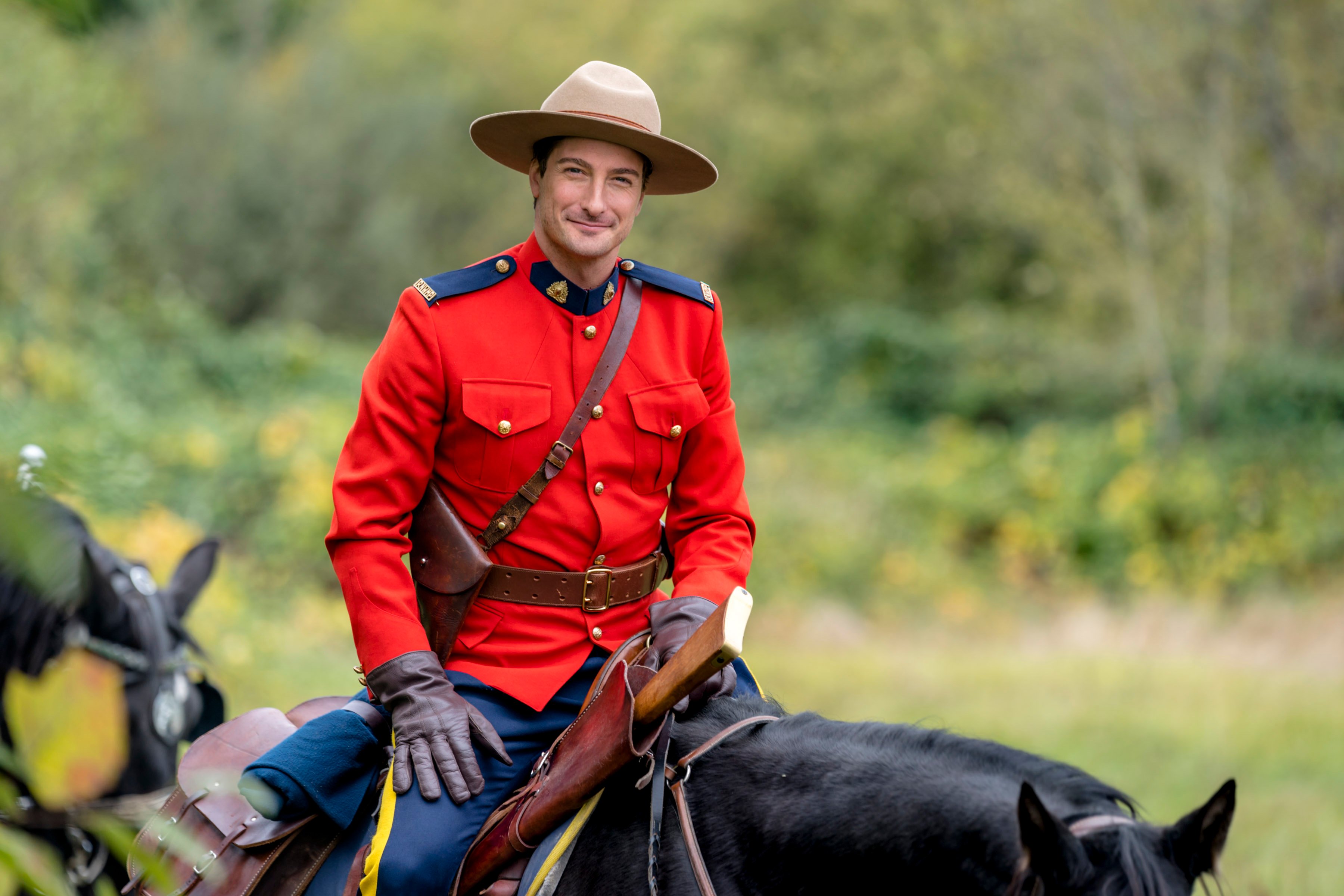 Daniel Lissing as Jack Thornton wearing a red jacket and hat and riding a horse in 'When Calls the Heart'