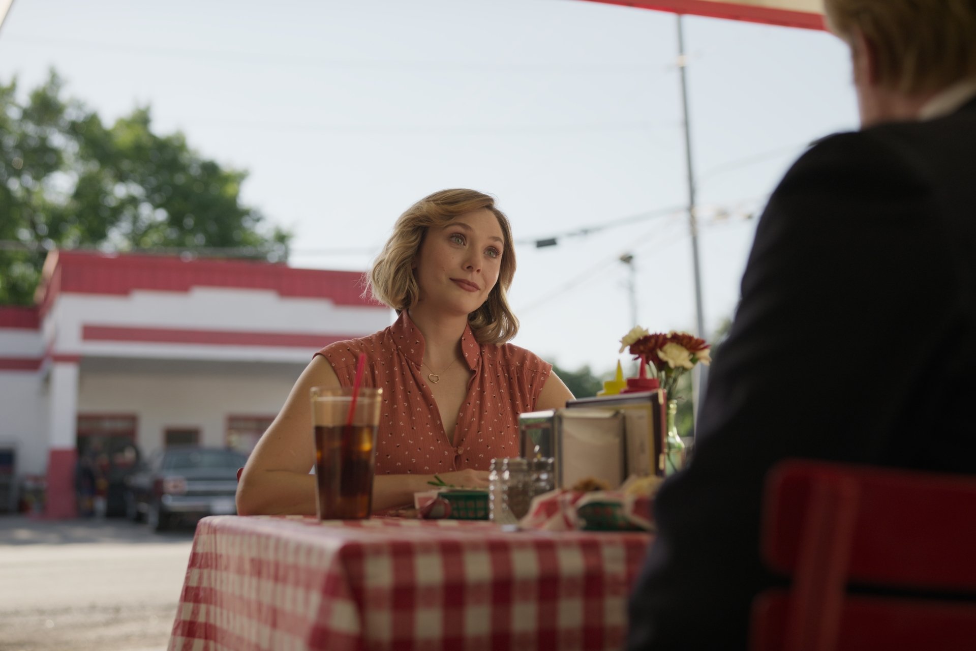 Elizabeth Olsen, sitting outside at a picnic table in 'Love & Death'