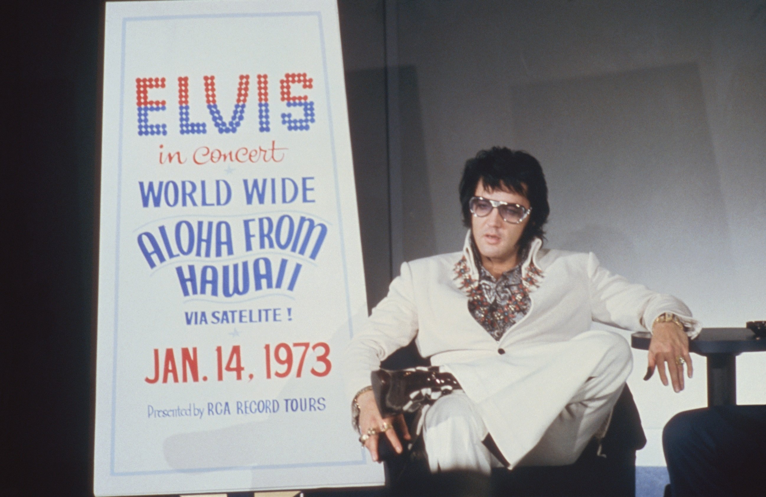 Elvis Presley sitting near a poster in Las Vegas