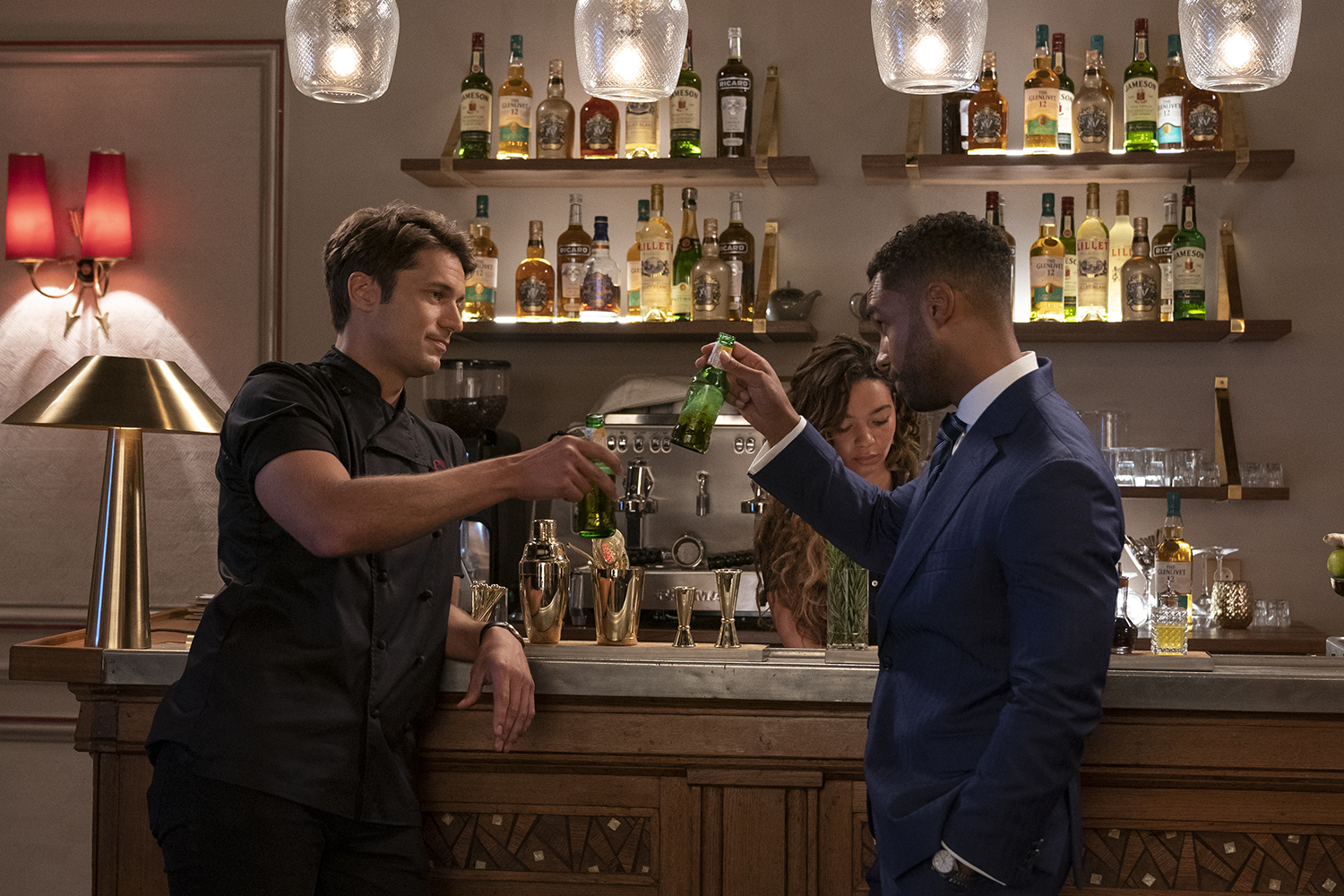 Lucas Braco as Gabriel and Lucien Laviscount as Alfie making a cheers gesture at a bar in Emily in Paris.