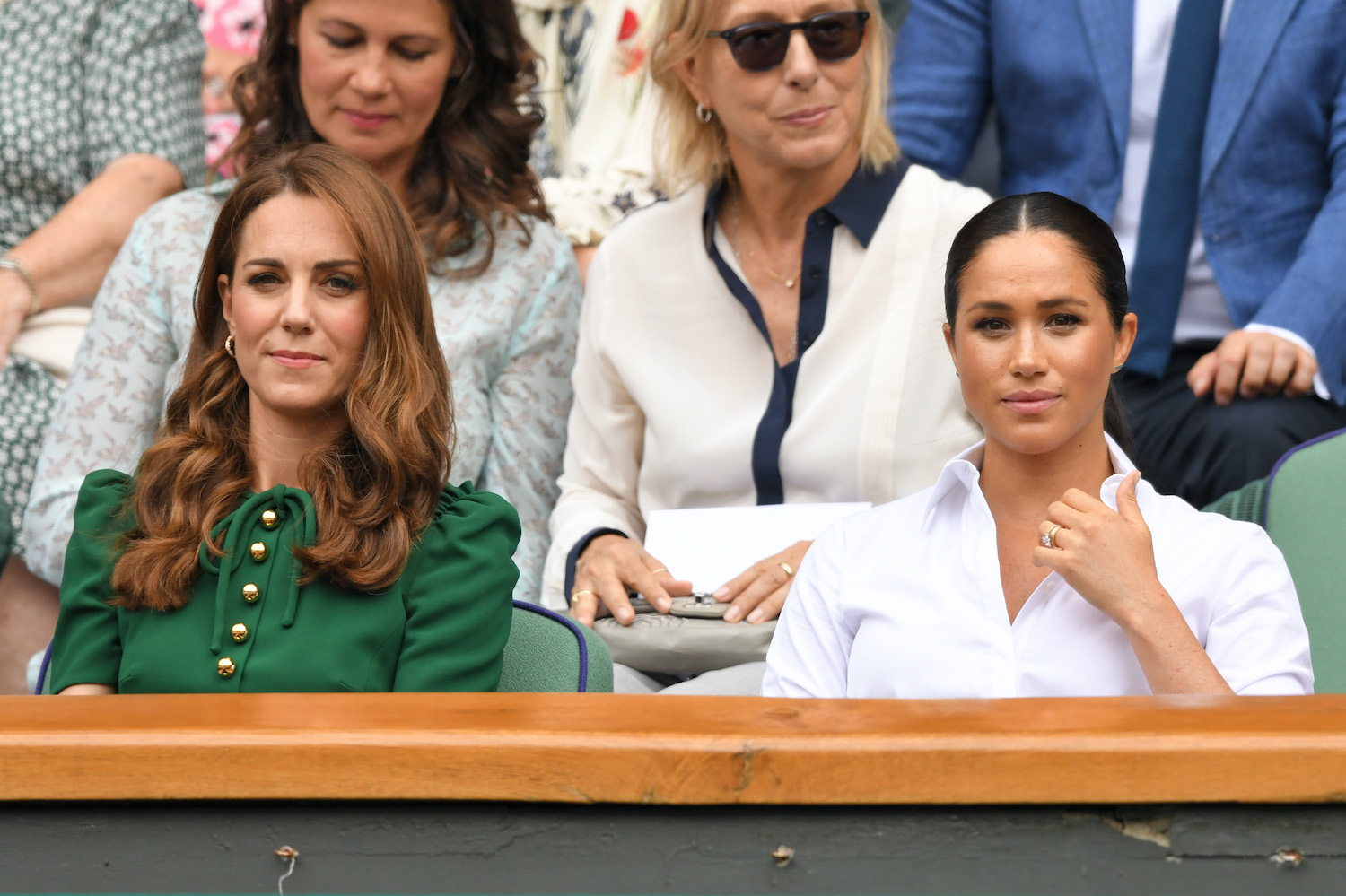Kate Middleton and Meghan Markle sit together at Wimbledon in 2019 with Kate wearing a green dress and Meghan wearing a white top.