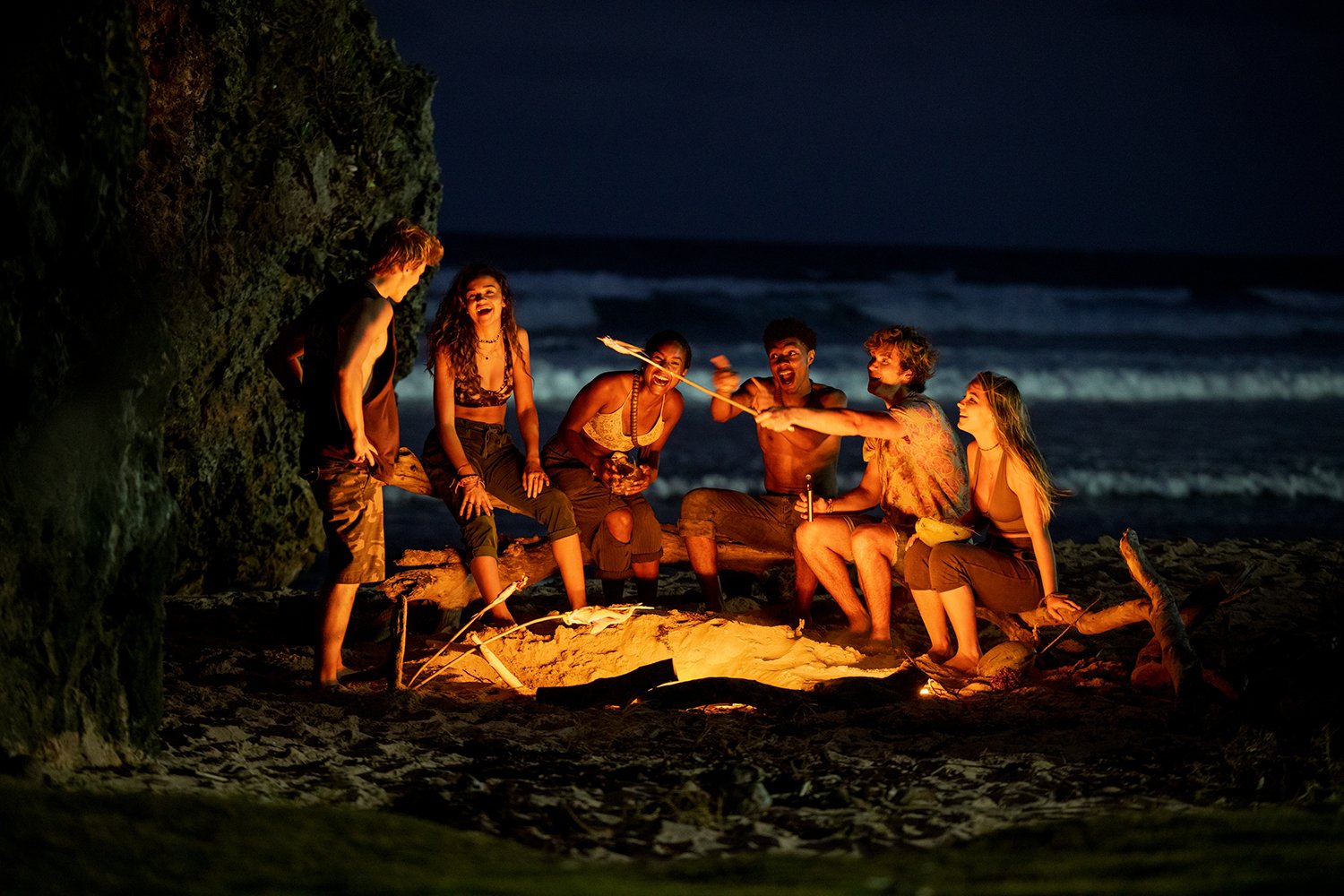 Rudy Pankow as JJ, Madison Bailey as Kiara, Carlacia Grant as Cleo, Jonathan Daviss as Pope, Chase Stokes as John B, and Madelyn Cline as Sarah Cameron sit around a fire on a beach in Outer Banks Season 2.