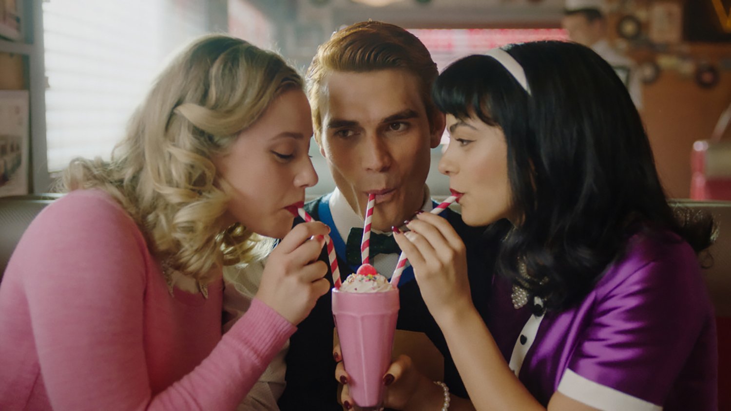 Lili Reinhart as Betty Cooper, KJ Apa as Archie Andrews, and Camila Mendes as Veronica Lodge sip from a milkshake during the 100th episode of Riverdale