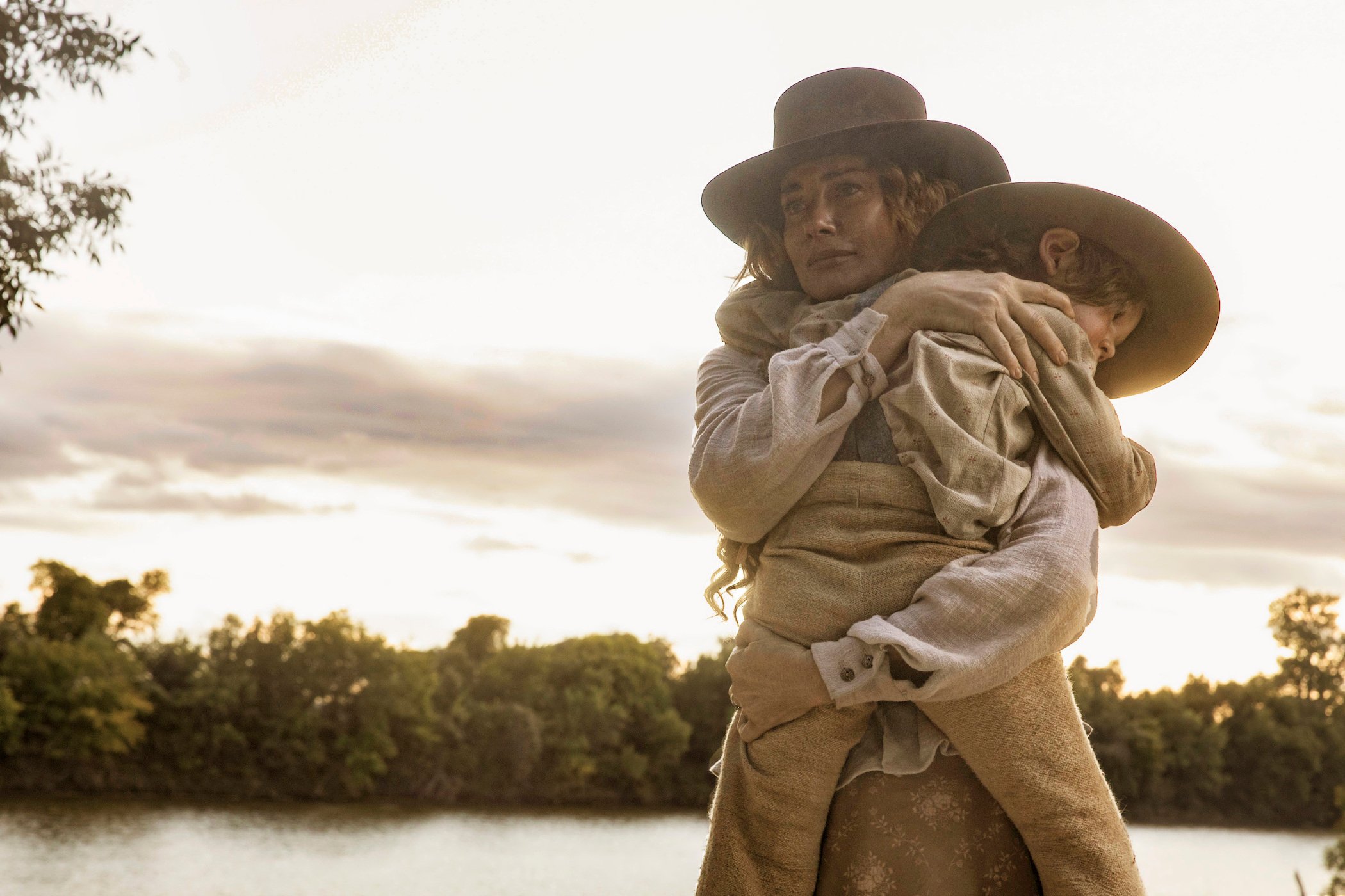 Faith Hill in '1883' holding a child in her arms with a lake behind her