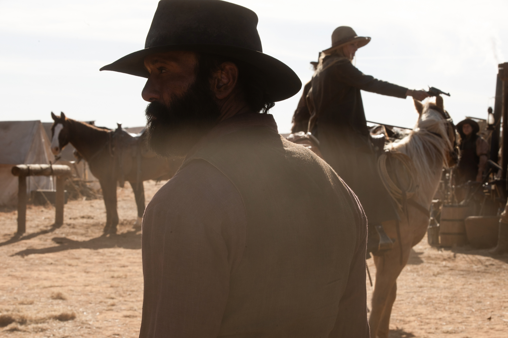 A close-up of Tim McGraw as James Dutton in '1883' with horses and people on the horses behind him