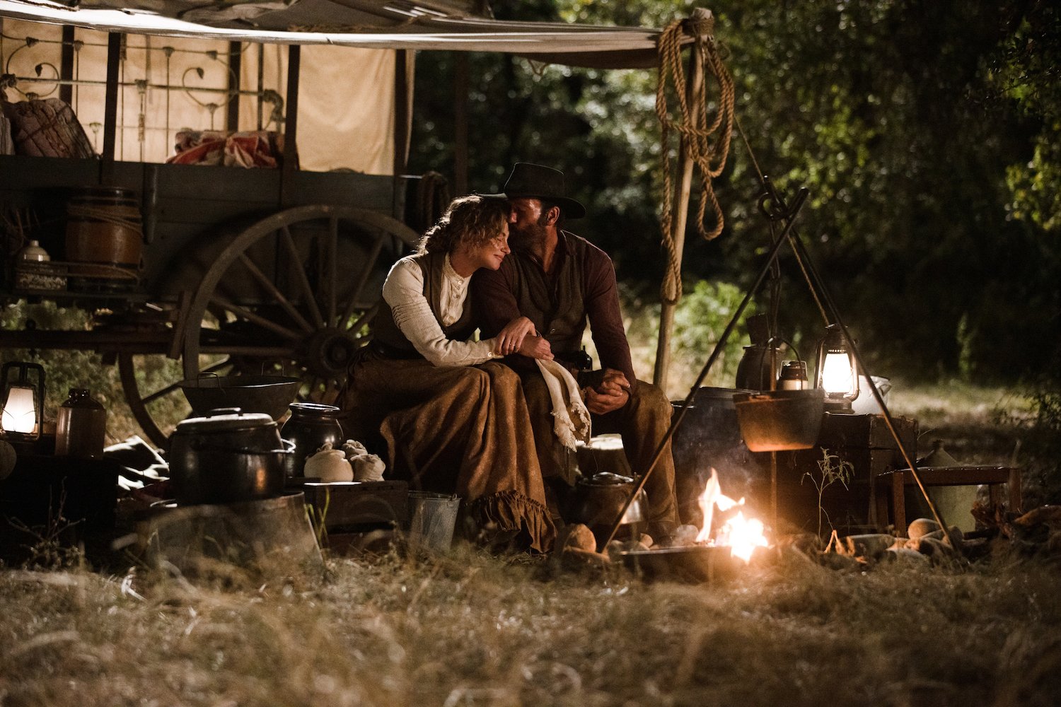 Faith Hill as Margaret Dutton and Tim McGraw as James Dutton sitting next to each other by a fire in '1883' 