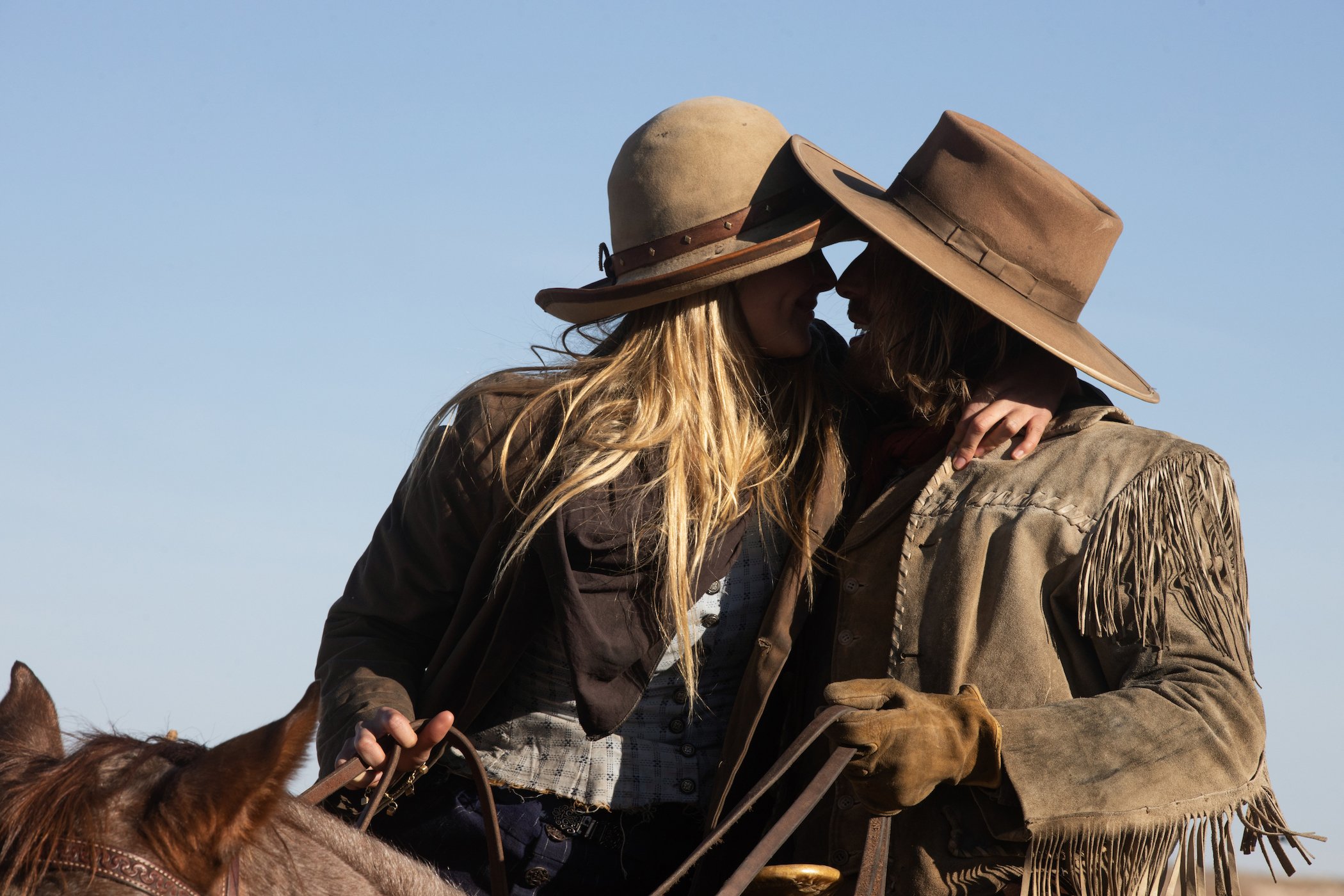 Isabel May as Elsa Dutton and Eric Nelsen as Ennis about to kiss each other while riding horses in '1883'