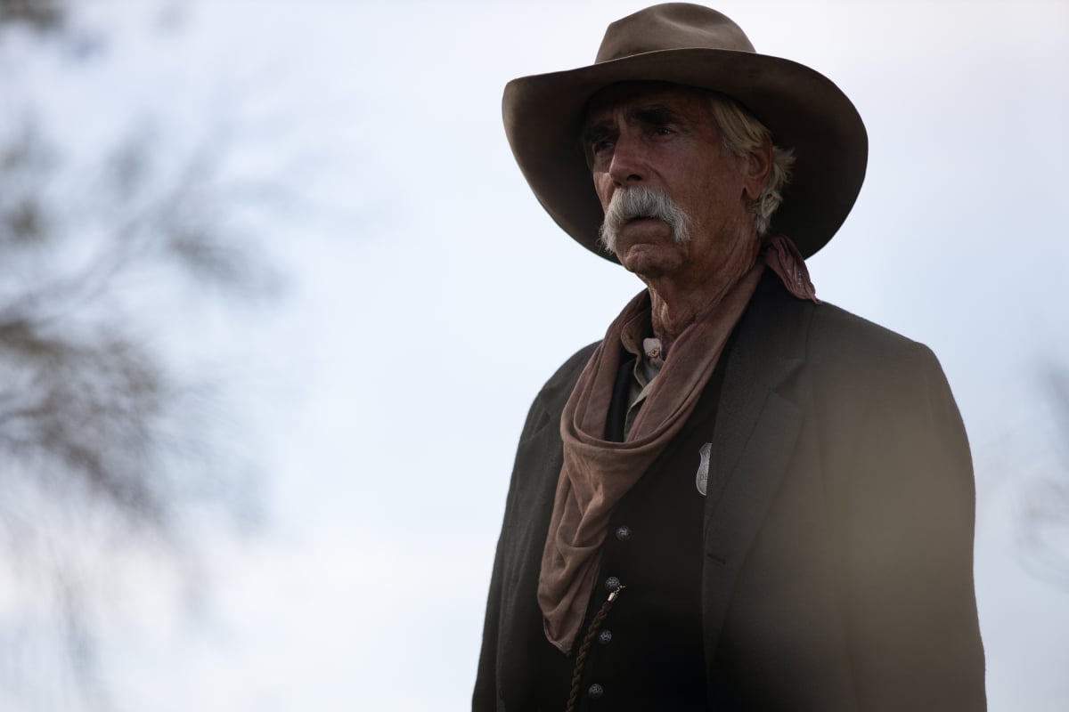 Sam Elliott as Shea of the Paramount+ original series 1883. Shea wears a cowboy hat, jacket, and black button-down shirt.