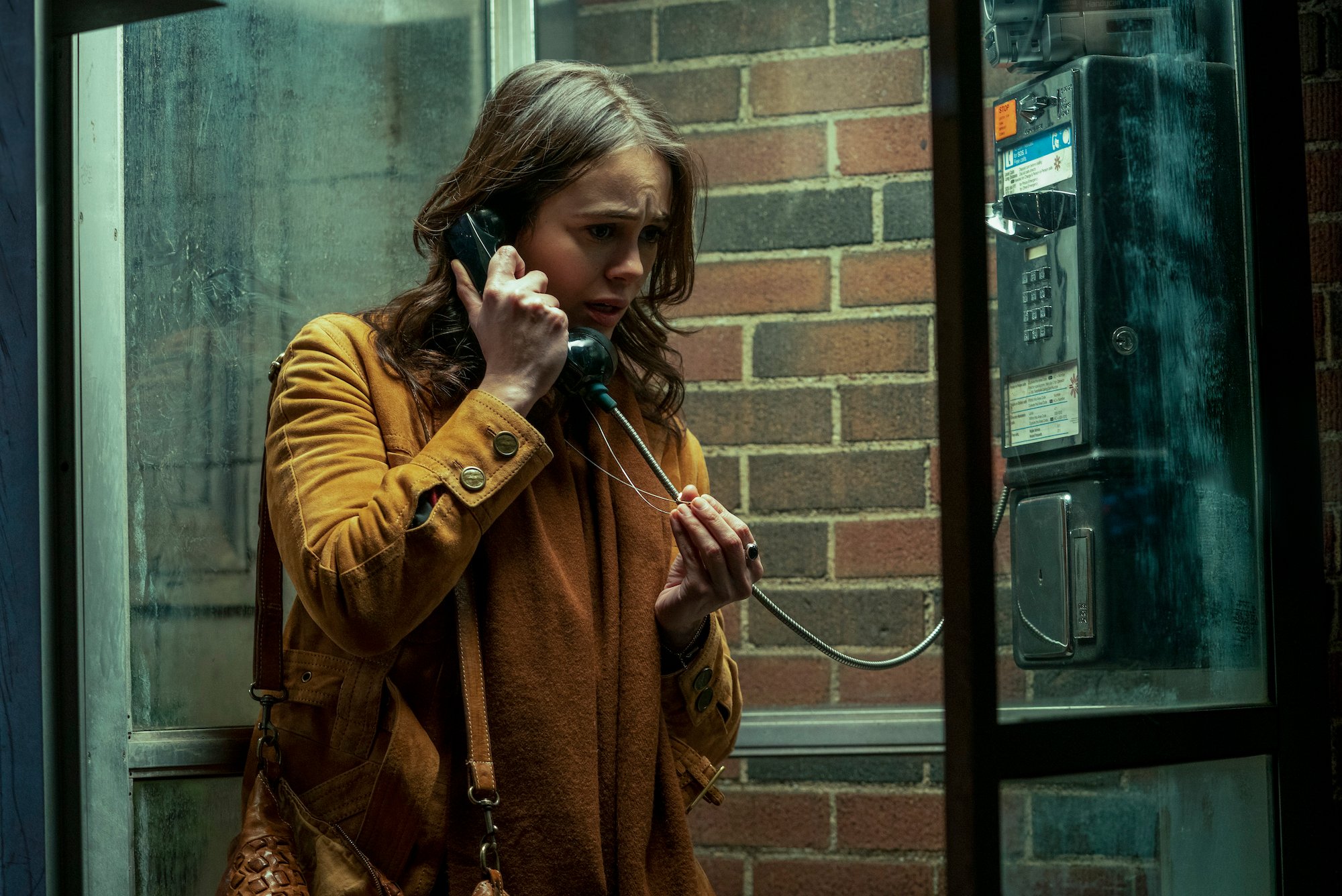 Dina Shihabi as Melody Pendras talking on a payphone and wearing a mustard colored jacket in a production still from 'Archive 81.'