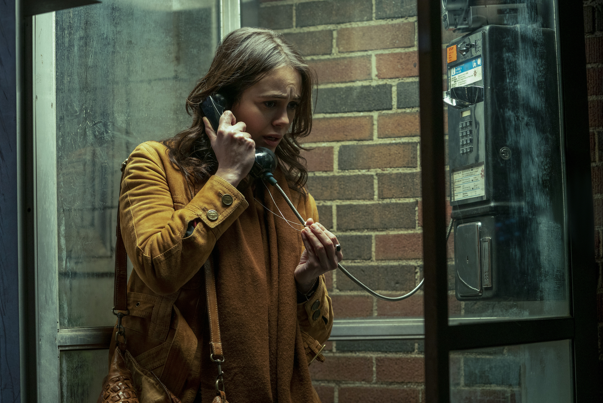 Dina Shihabi as Melody Pendras talking on a payphone and wearing a mustard colored jacket in a production still from 'Archive 81.'