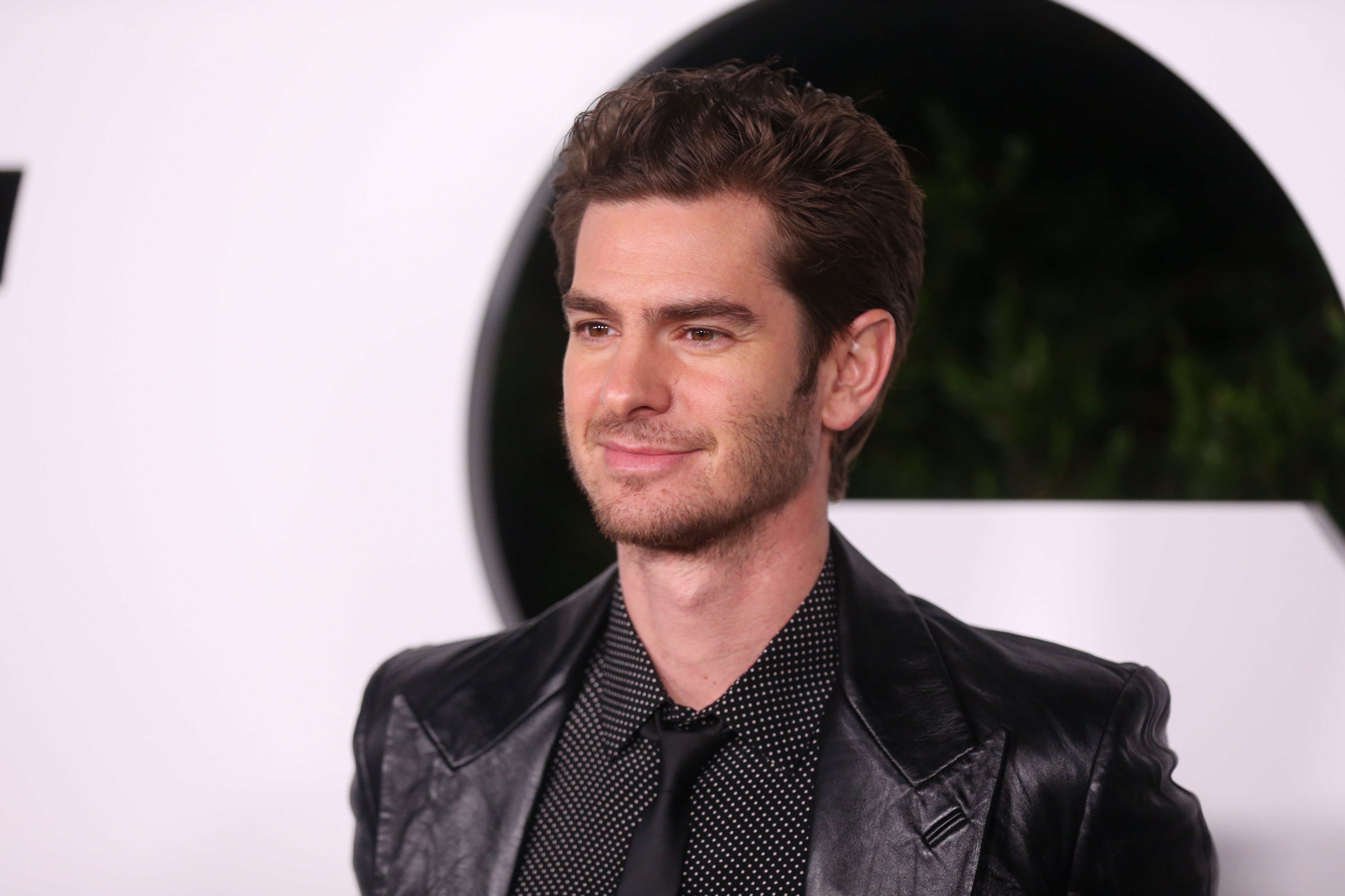 'Spider-Man: No Way Home' star Andrew Garfield wears a black leather blazer over a black button-up shirt with white polka dots and a black tie.