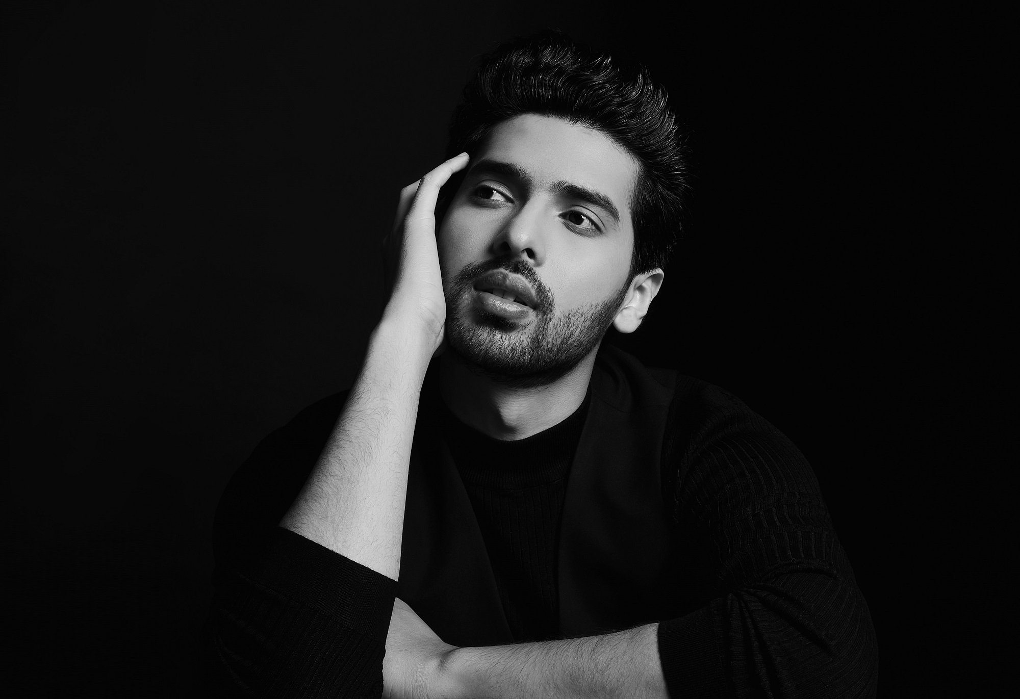 Armaan Malik touches the side of his face in a black-and-white photo