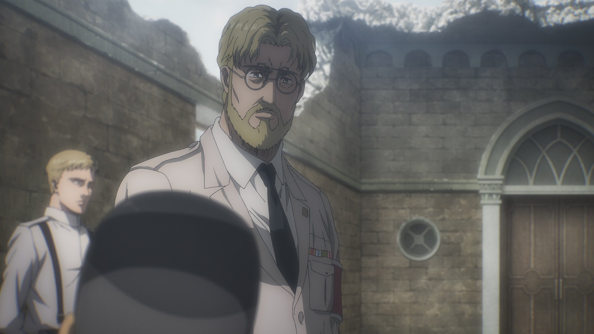 Zeke Jaeger in 'Attack on Titan' Season 4 Part 1. He's wearing a beige uniform and looking down at someone.