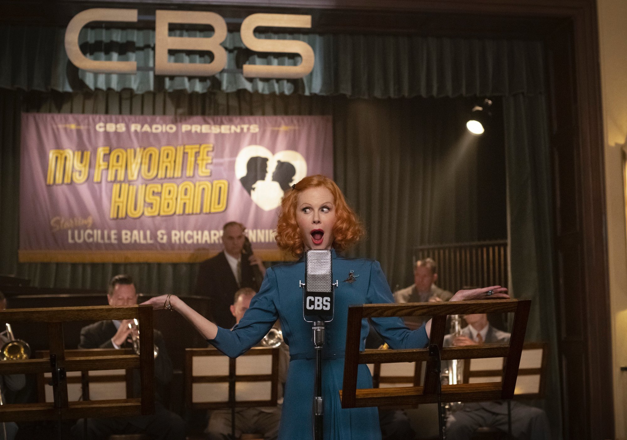 'Being the Ricardos' Nicole Kidman as Lucille Ball holding her hands up behind a microphone in front of the CBS logo