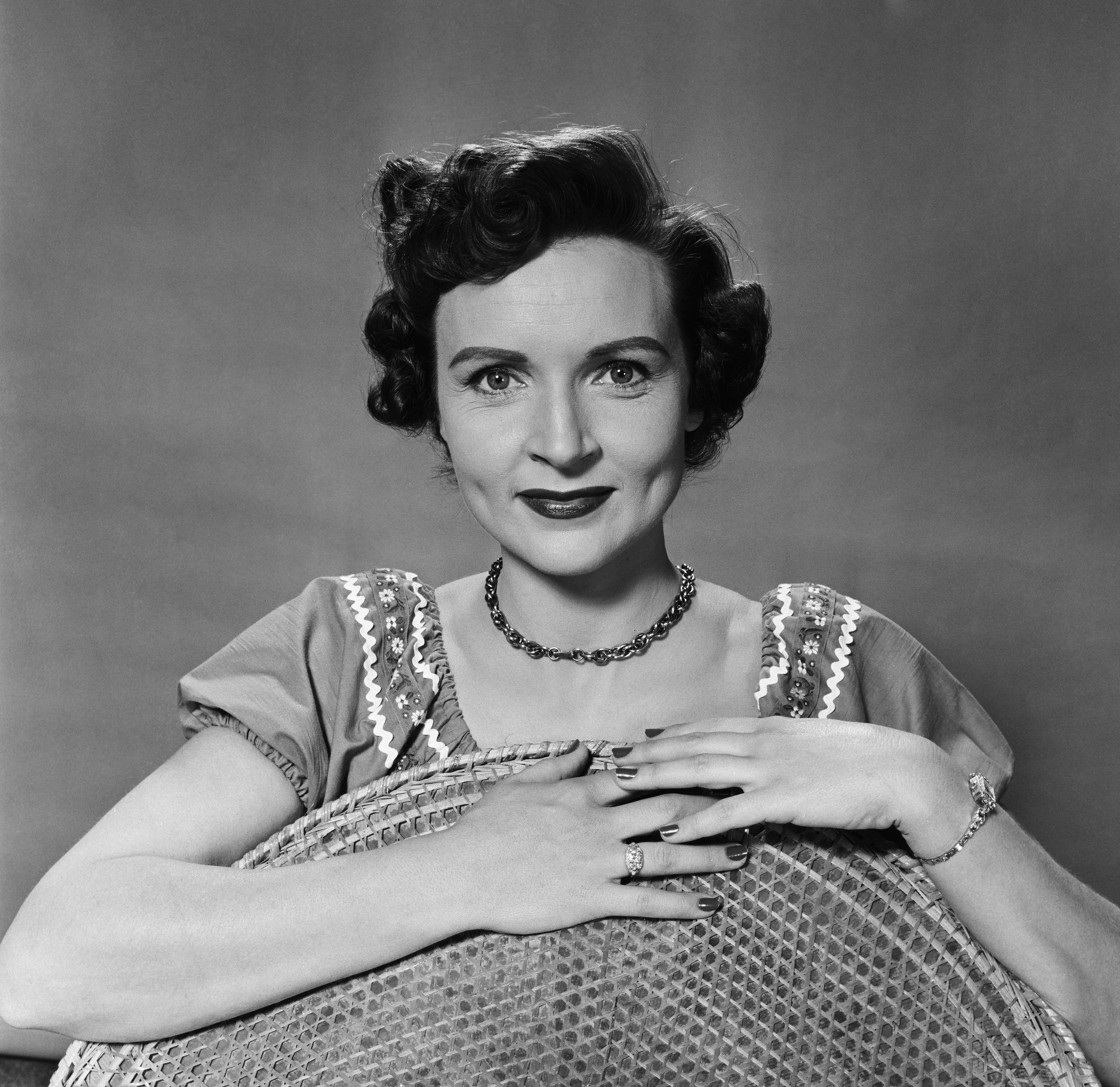 Betty White poses while holding the back of a wicker chair