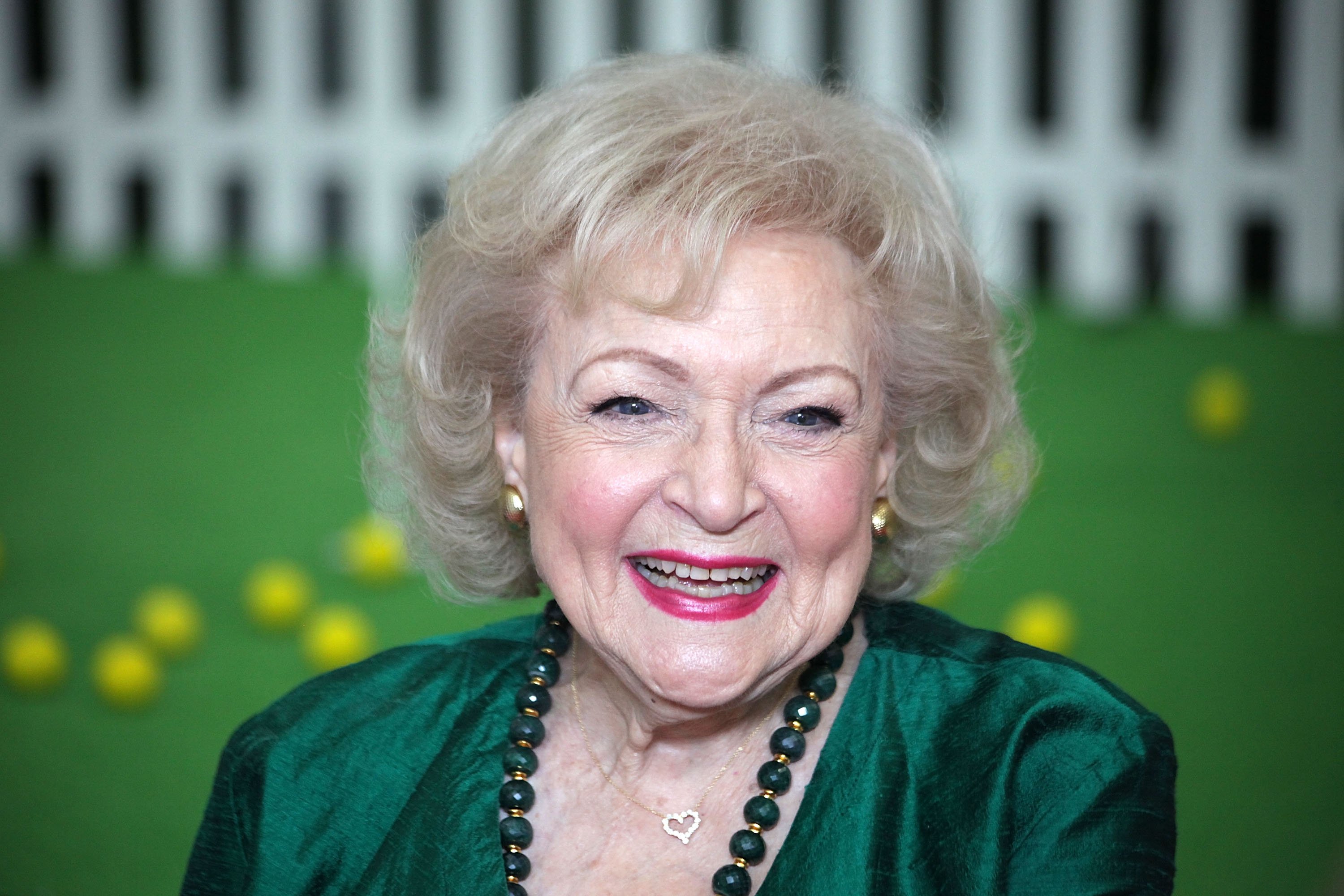 Betty White smiles while wearing a green dress and matching green earrings.