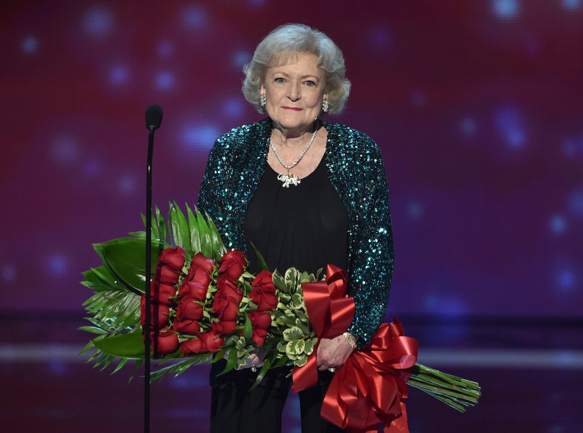 Betty White wears green and black while holding a bouquet of roses