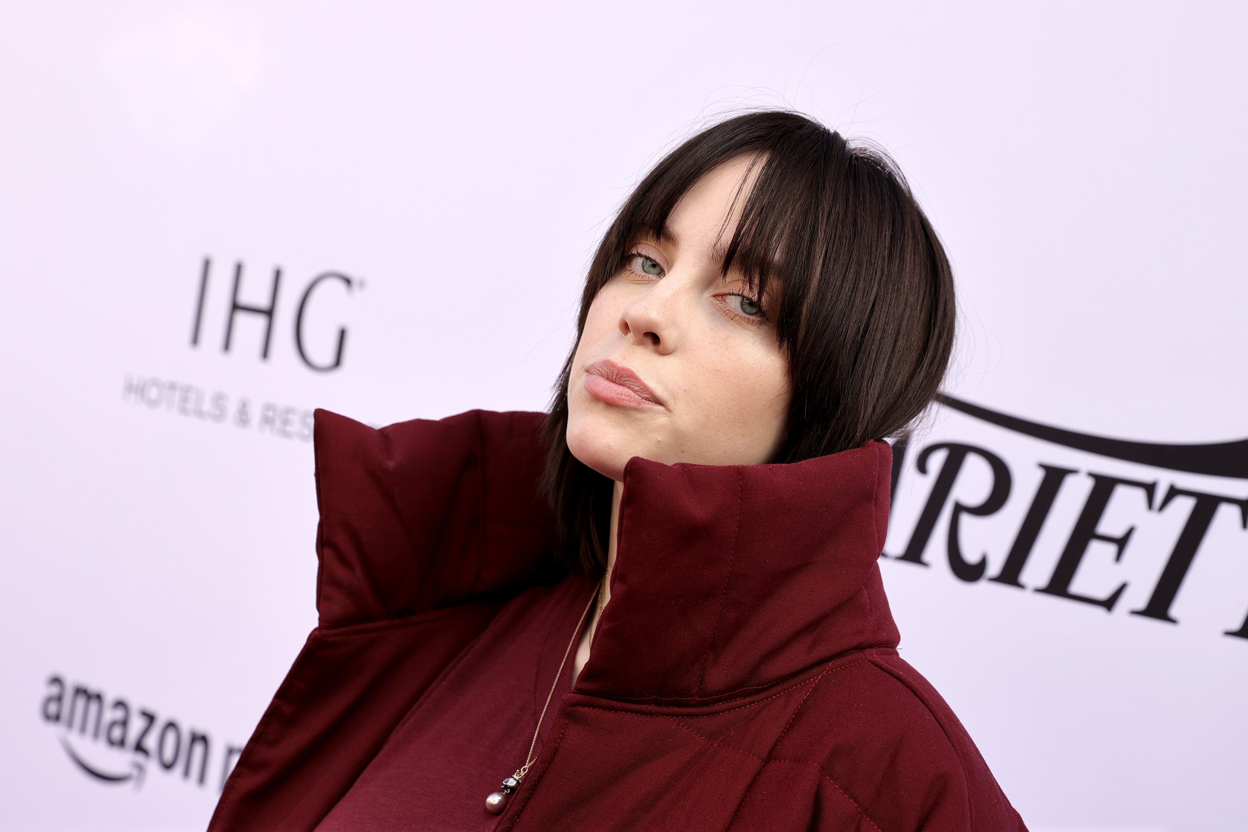 Billie Eilish attends Variety's Hitmakers Brunch presented by Peacock and Girls5eva dressed in a dark red coat and shirt with brown hair