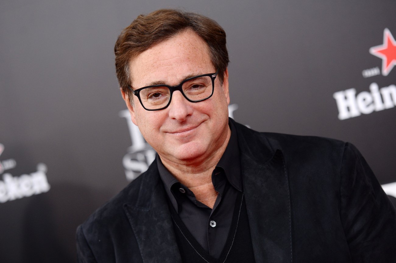 Bob Saget wearing glasses in front of a gray background