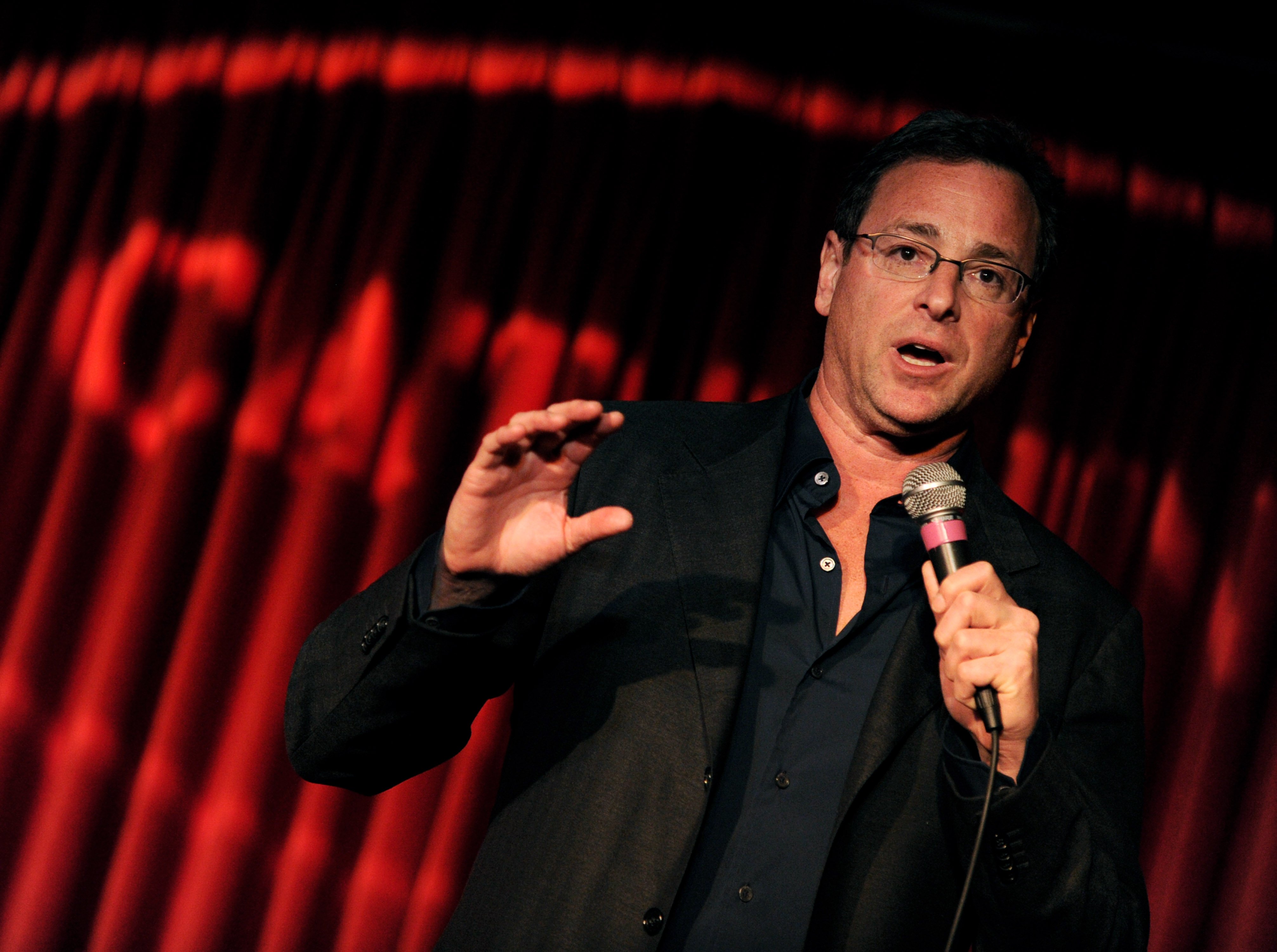 Bob Saget holding a microphone and performing