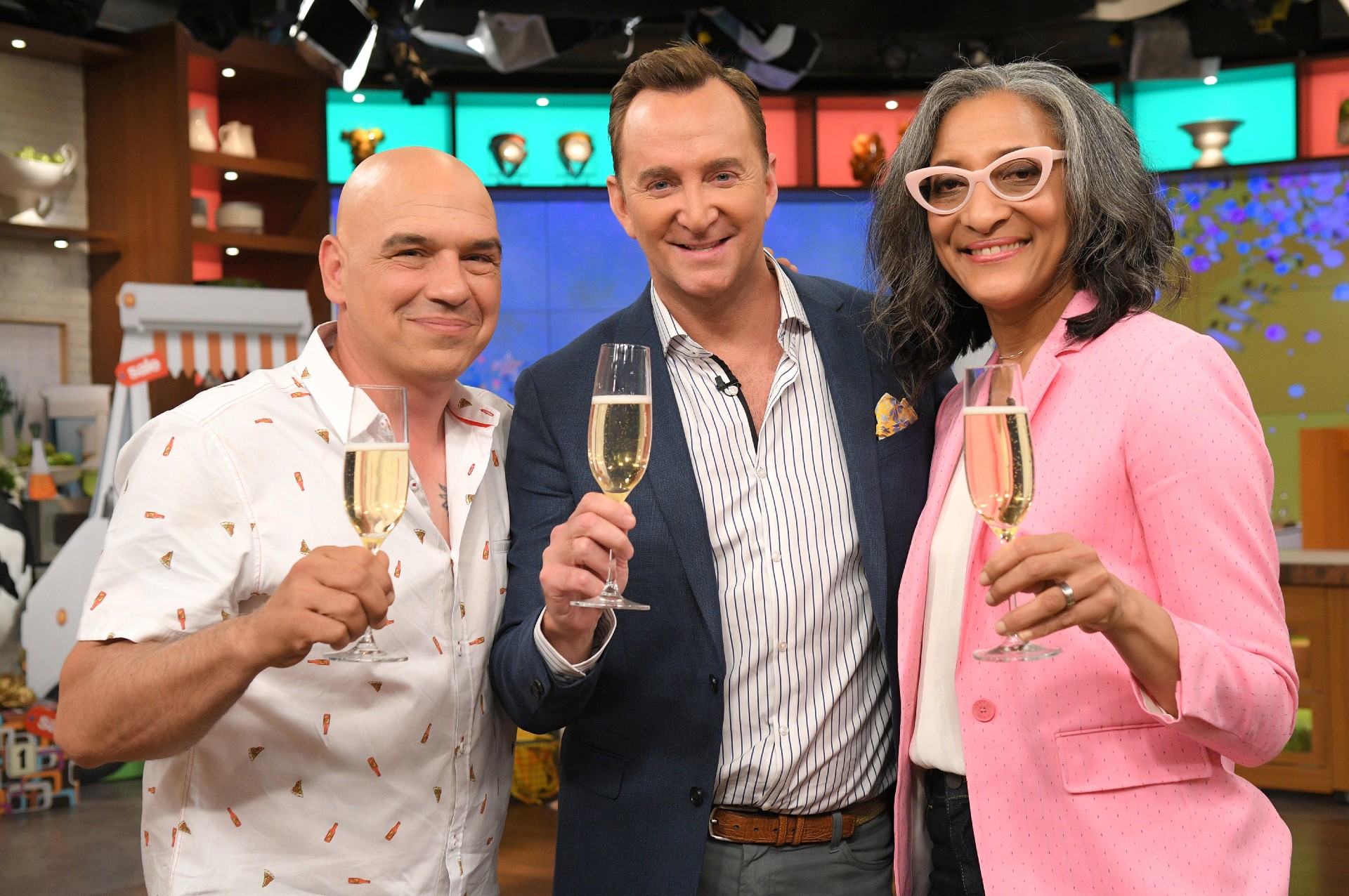 Michael Symon, Clinton Kelly, and Carla Hall raise a glass of wine on the set of The Chew