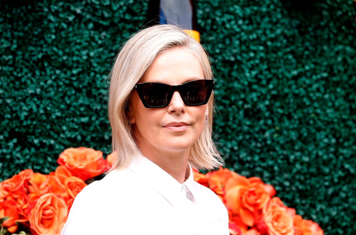 Charlize Theron posing while wearing a white dress and sunglasses..