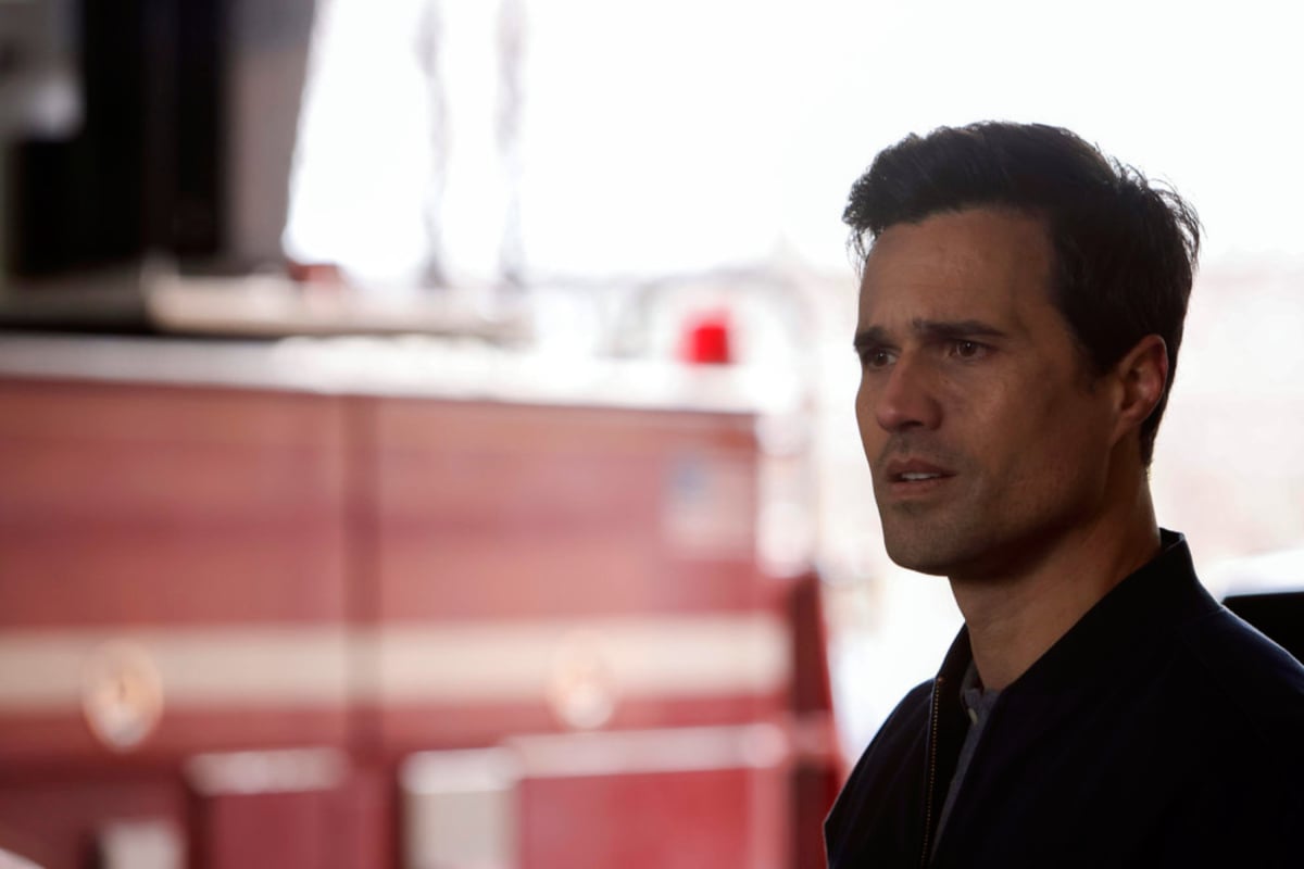Brett Dalton at Jason Pelham in Chicago Fire Season 10. Pelham stands in front of a fire truck and looks concerned. 