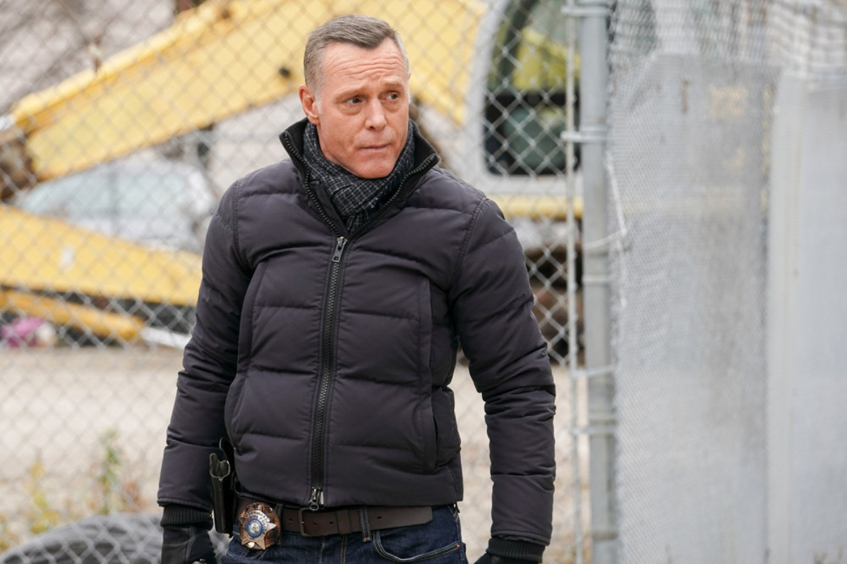 ason Beghe as Hank Voight in Chicago P.D. Season 9 Episode 12. Voight wears a black coat and stands in front of a chainlink fence.