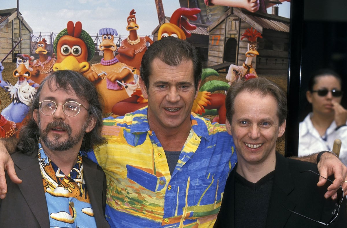 Peter Lord, Mel Gibson, and Nick Park pose in front of a ‘Chicken Run’ poster