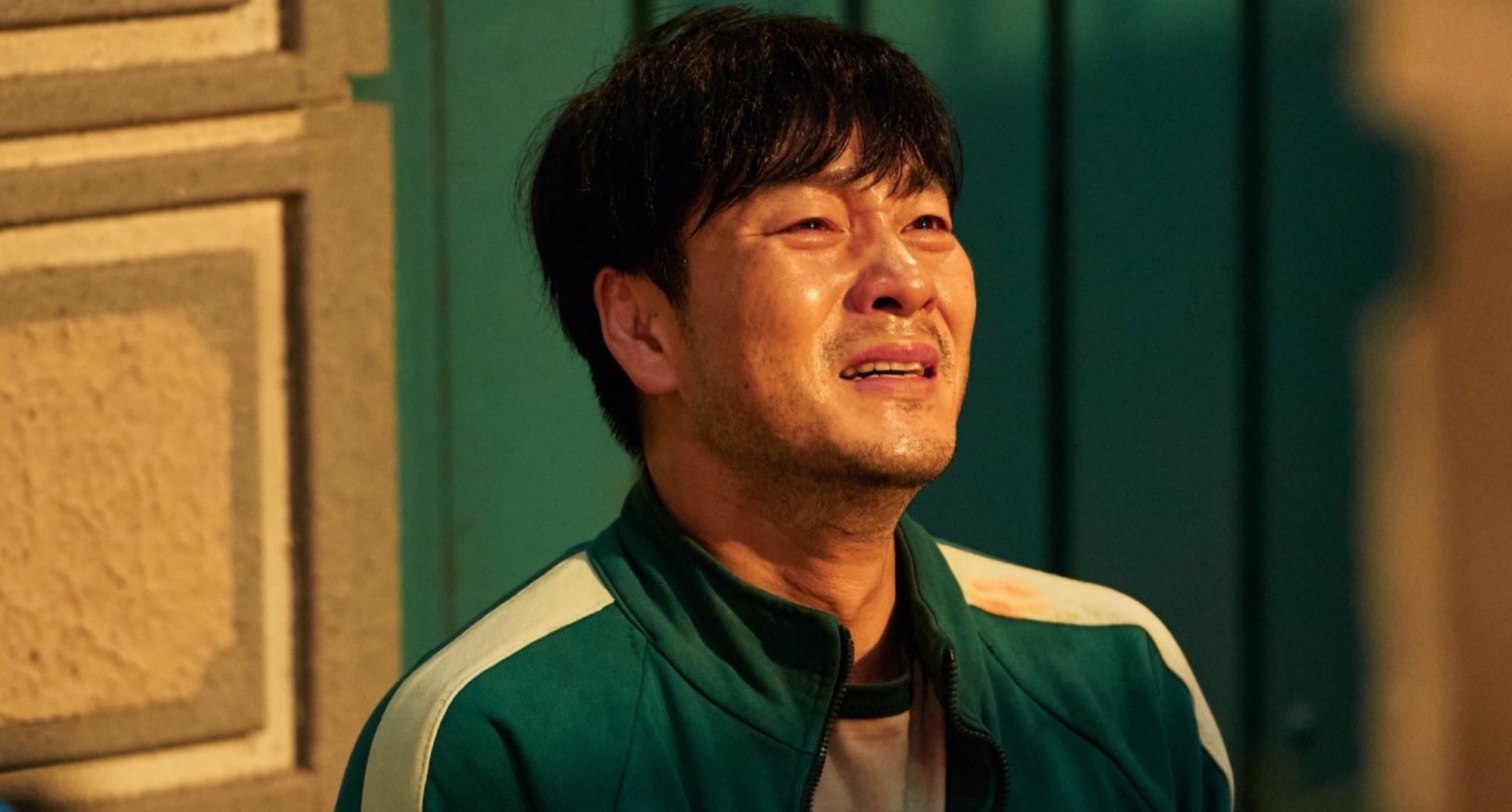 Cho Sang-woo from 'Squid Game' during marble game betrayal wearing green tracksuit and crying.