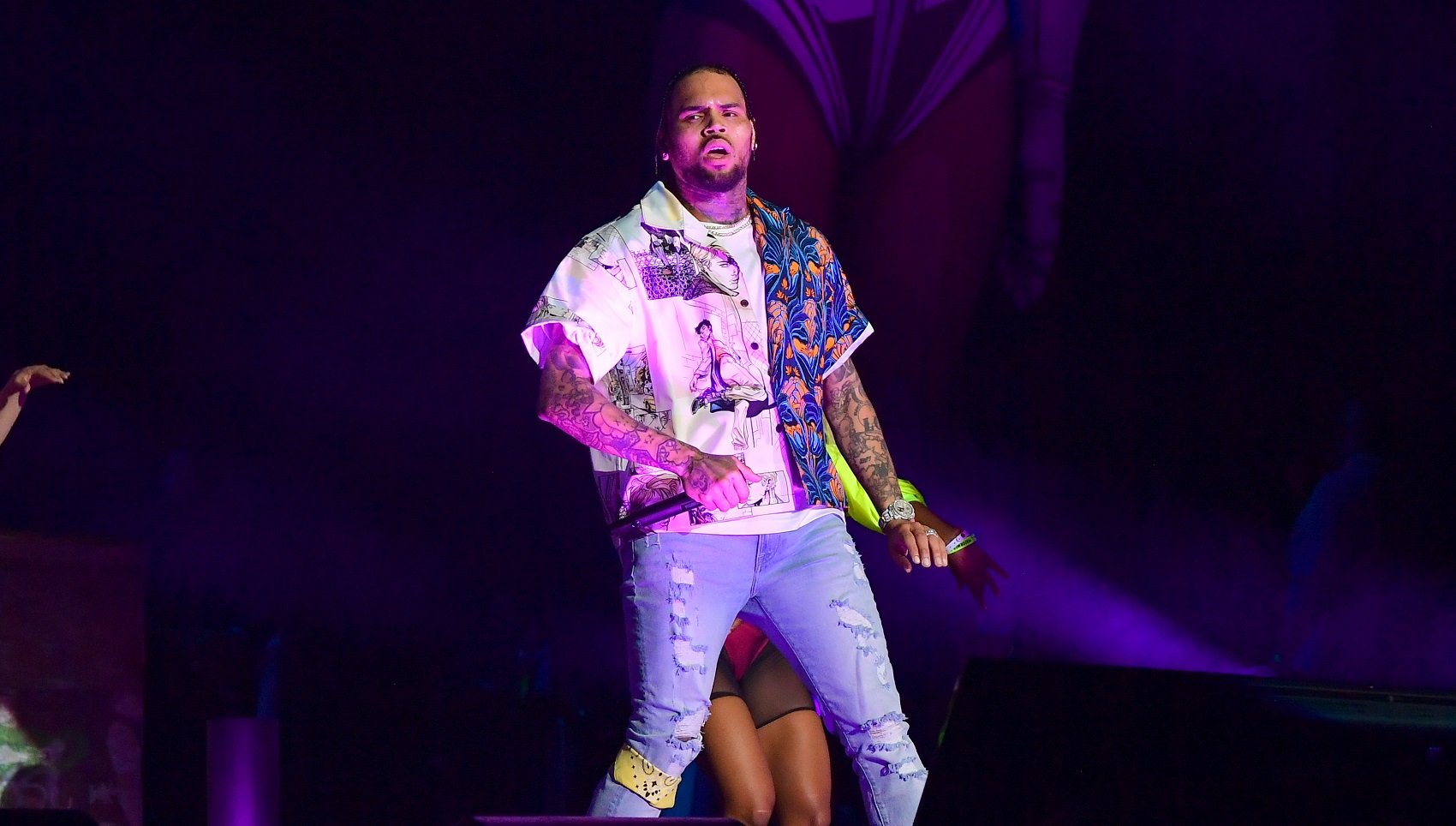 Chris Brown onstage in a multicolored shirt and a pair of skinny blue jeans