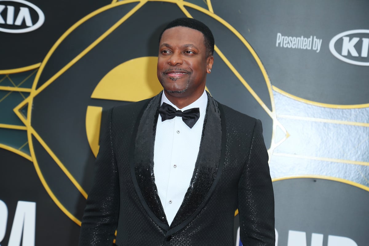 Chris Tucker wears a dark suit and smiles on the red carpet