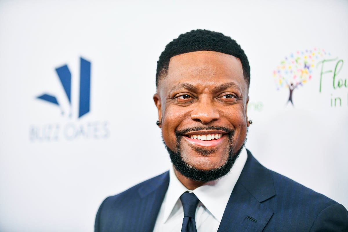 Chris Tucker wears a blue suit and smiles on the red carpet