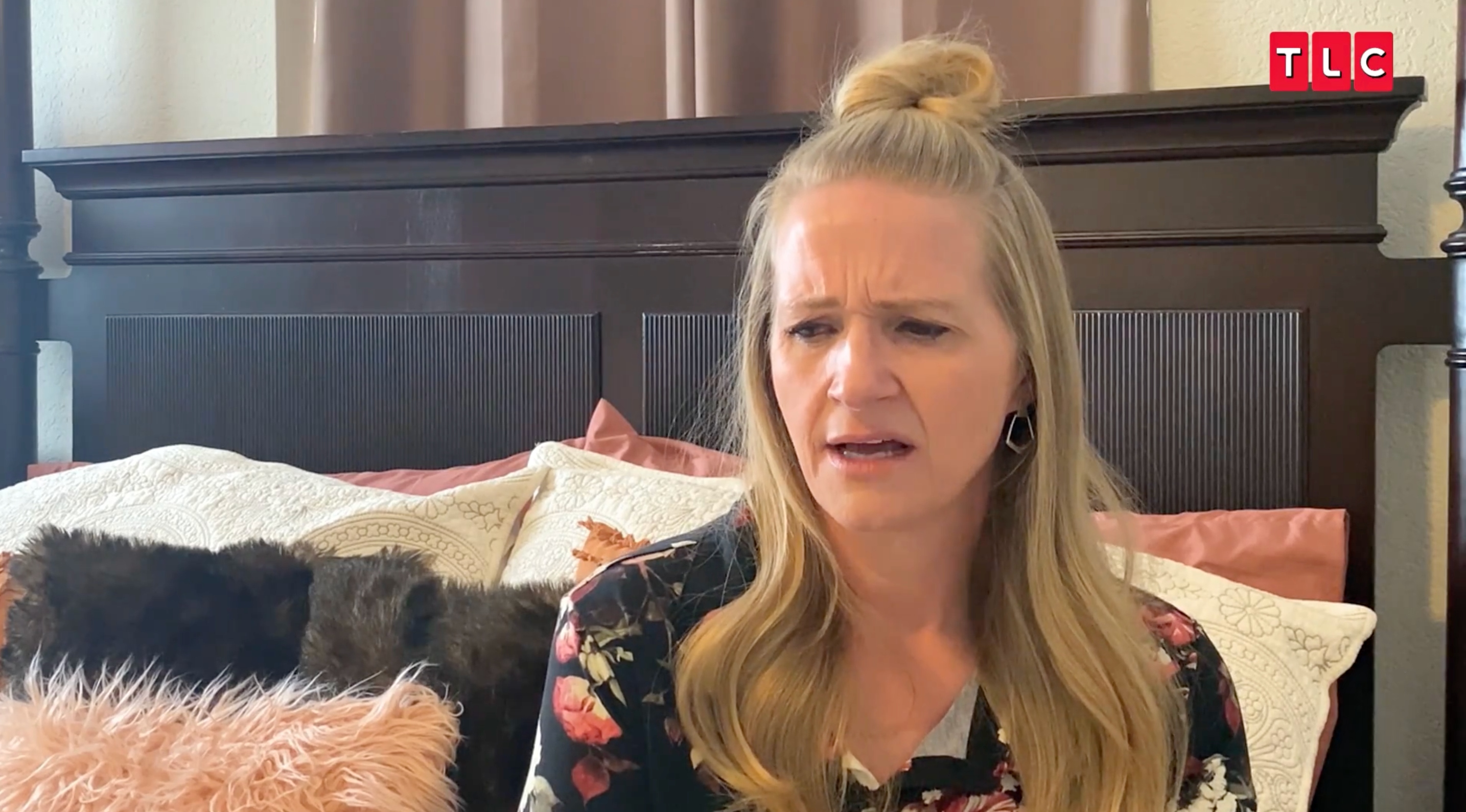 Christine Brown sitting on her bed, wearing a floral shirt on 'Sister Wives'.