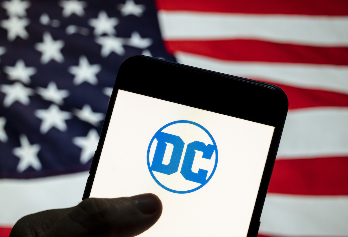 The DC Comics logo displayed on a smartphone with the U.S. flag in the background