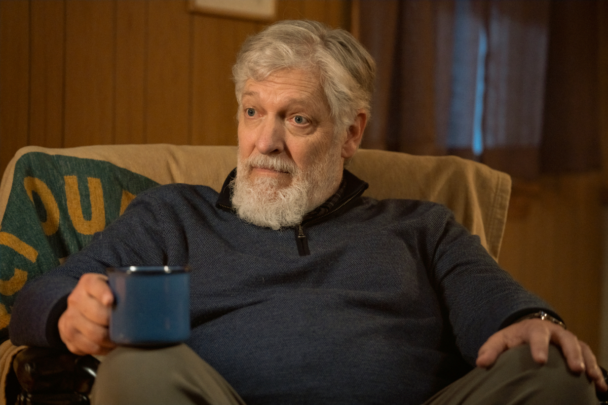 Clancy Brown as Kurt in Dexter: New Blood. Kurt sits in a chair and holds a mug. 