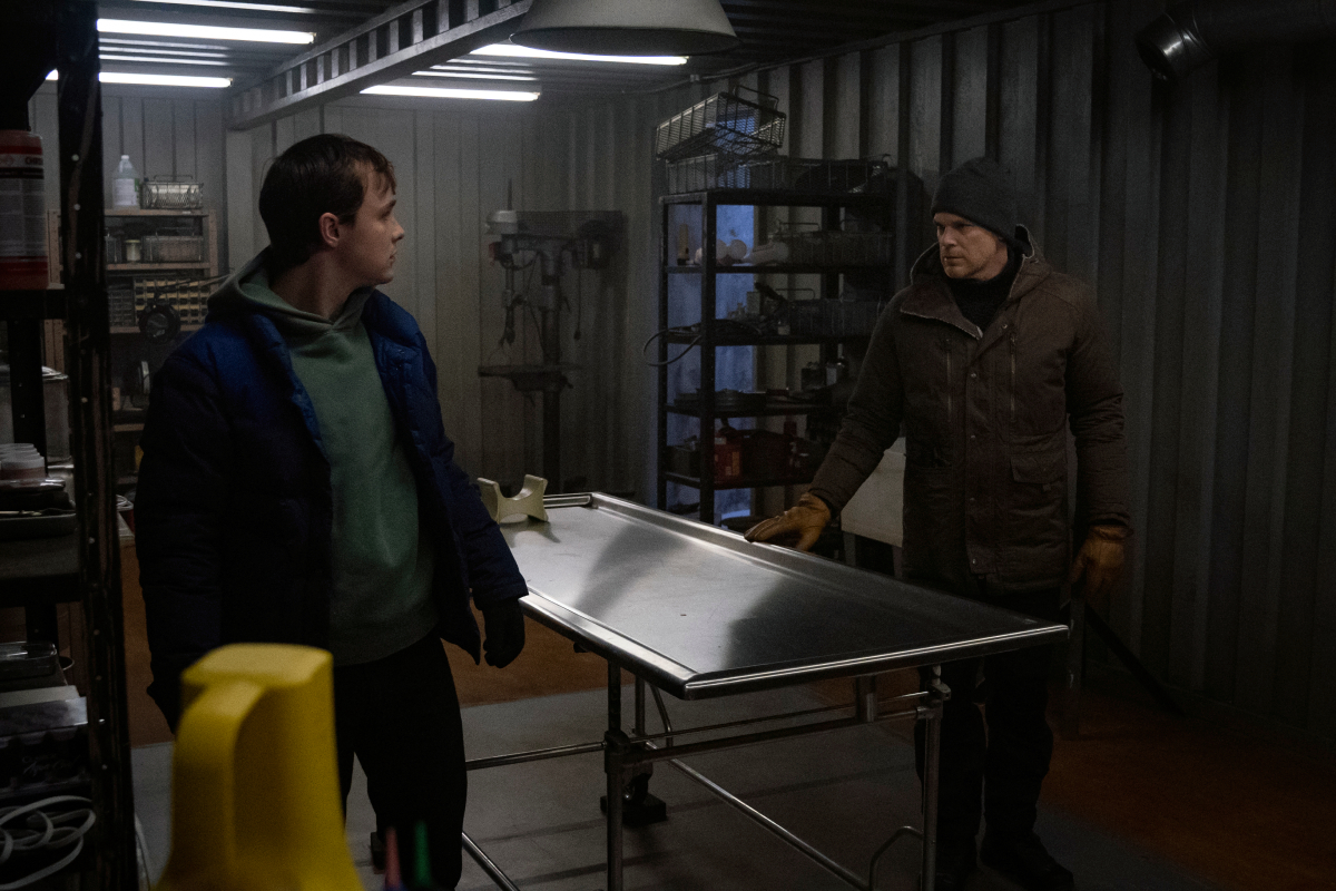 Jack Alcott as Harrison and Michael C. Hall as Dexter in Dexter: New Blood. Dexter and Harrison stand on either side of an empty kill table.