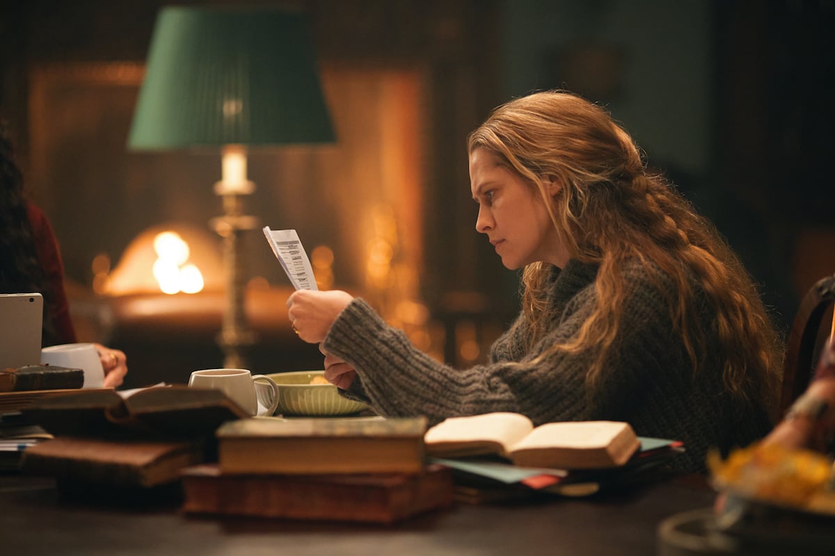 Diana sitting at a desk and looking at a piece of paper in 'A Discovery of Witches' Season 3