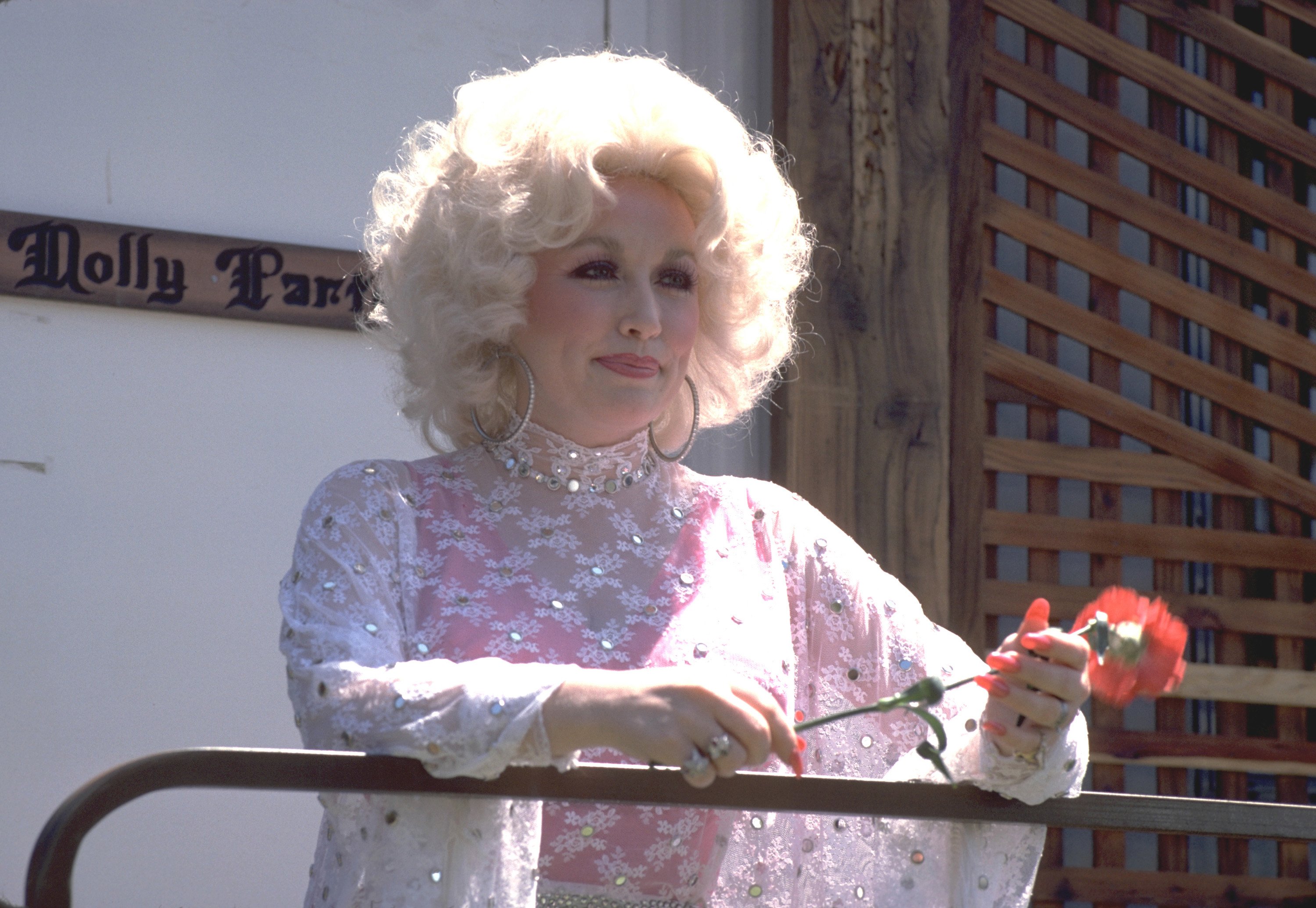 Dolly Parton wears a lace shirt and holds a flower.