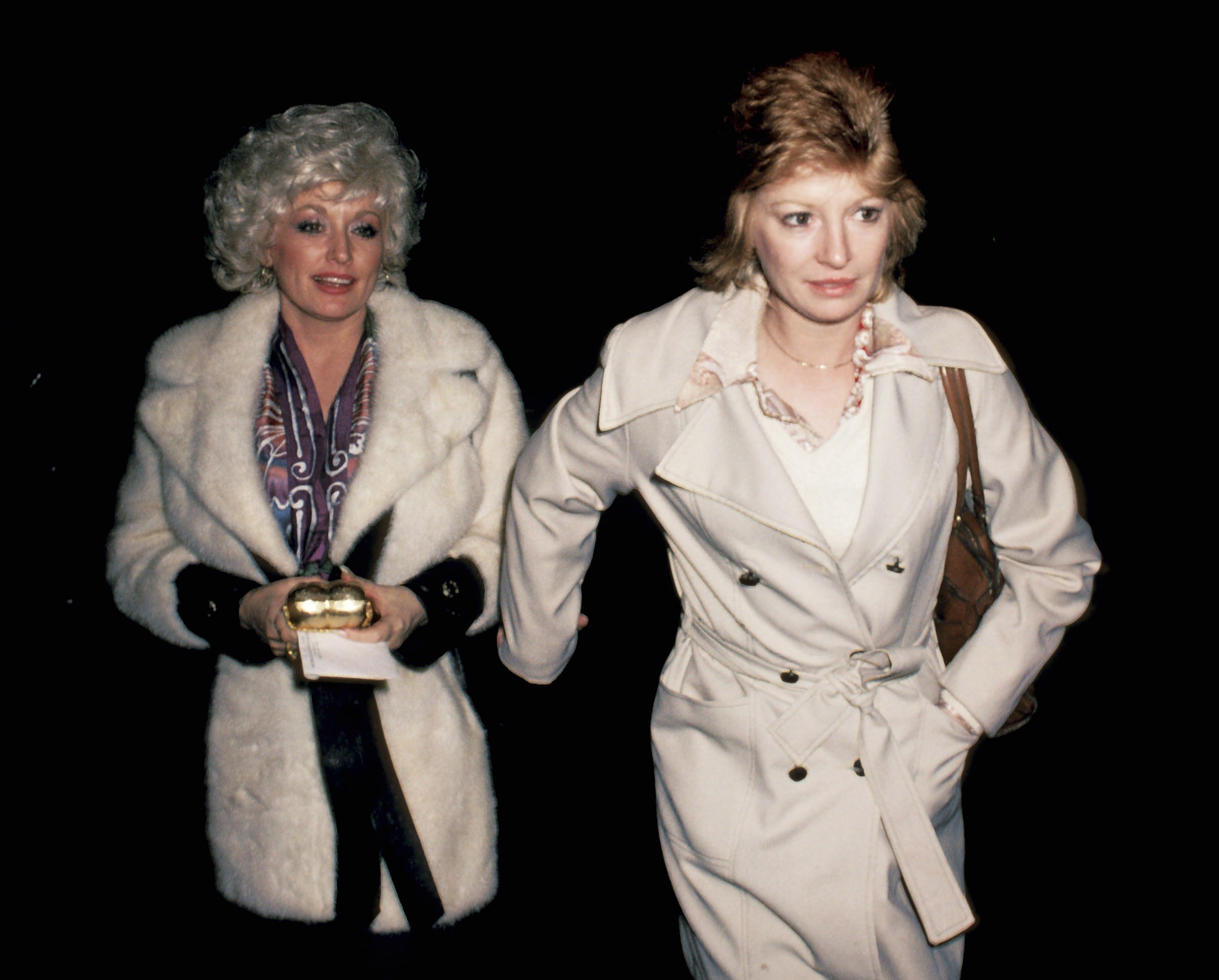 Dolly Parton and Judy Ogle wear tan coats and walk outside at night.