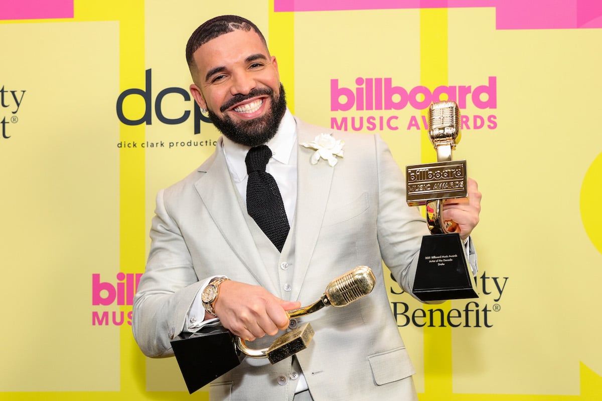 Drake smiles and holds two trophies at an event.